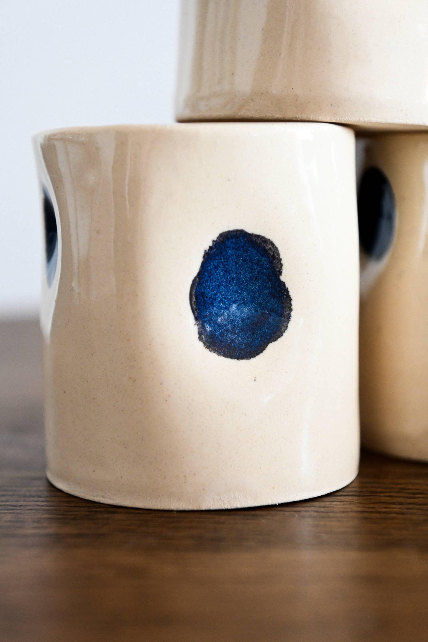 Le Soleil ceramic mug with cream glaze and blue dot detail on wood surface
