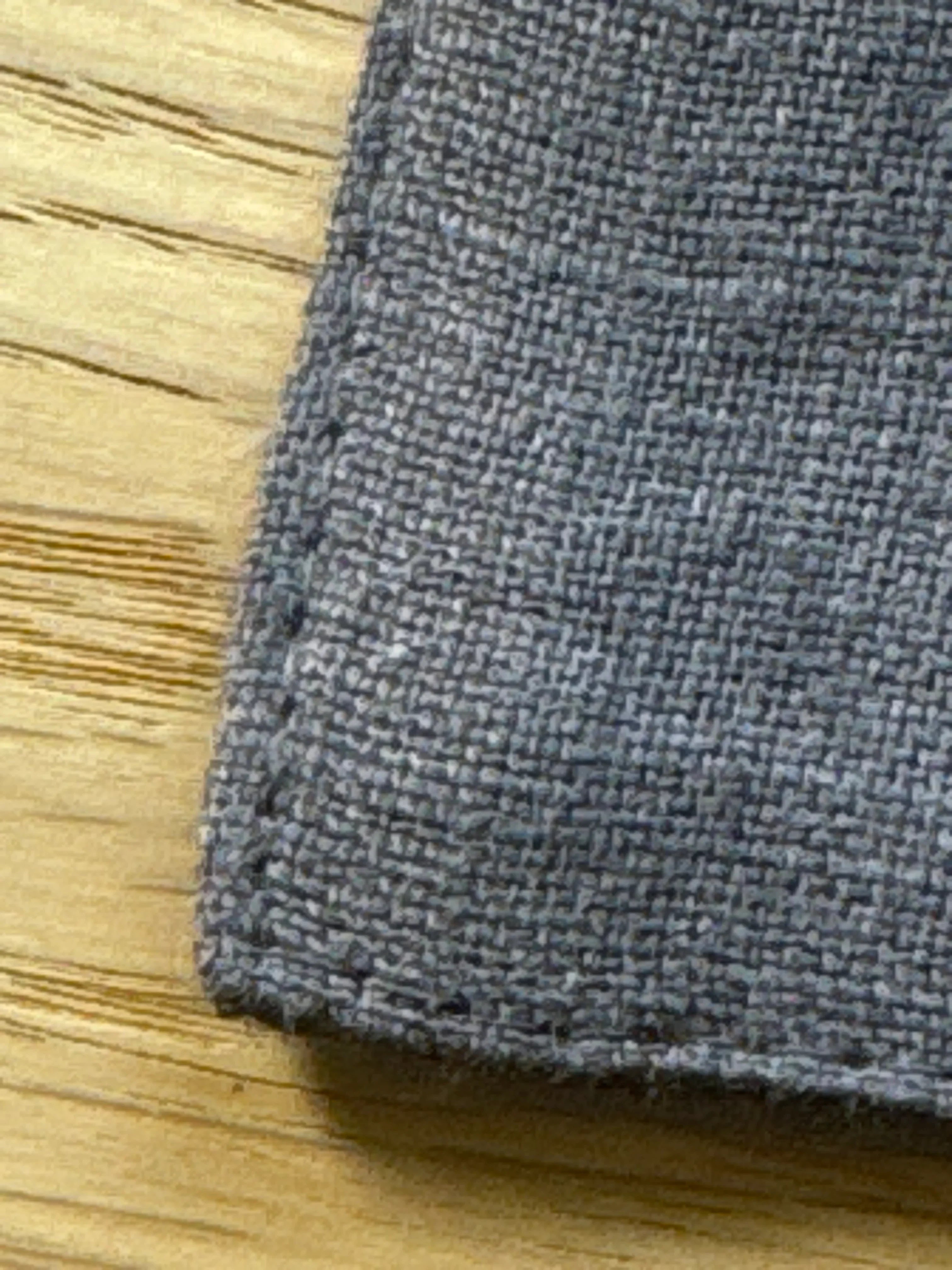 Wahtari grey linen napkin corner on light wood table, detailed stitching visible