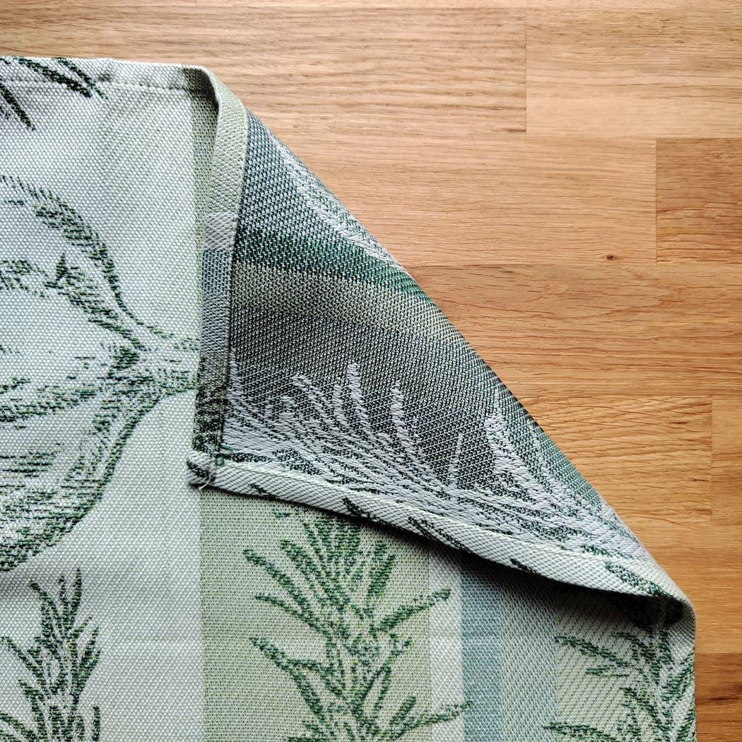 Jacquard woven cotton placemat with green botanical pattern on wooden table