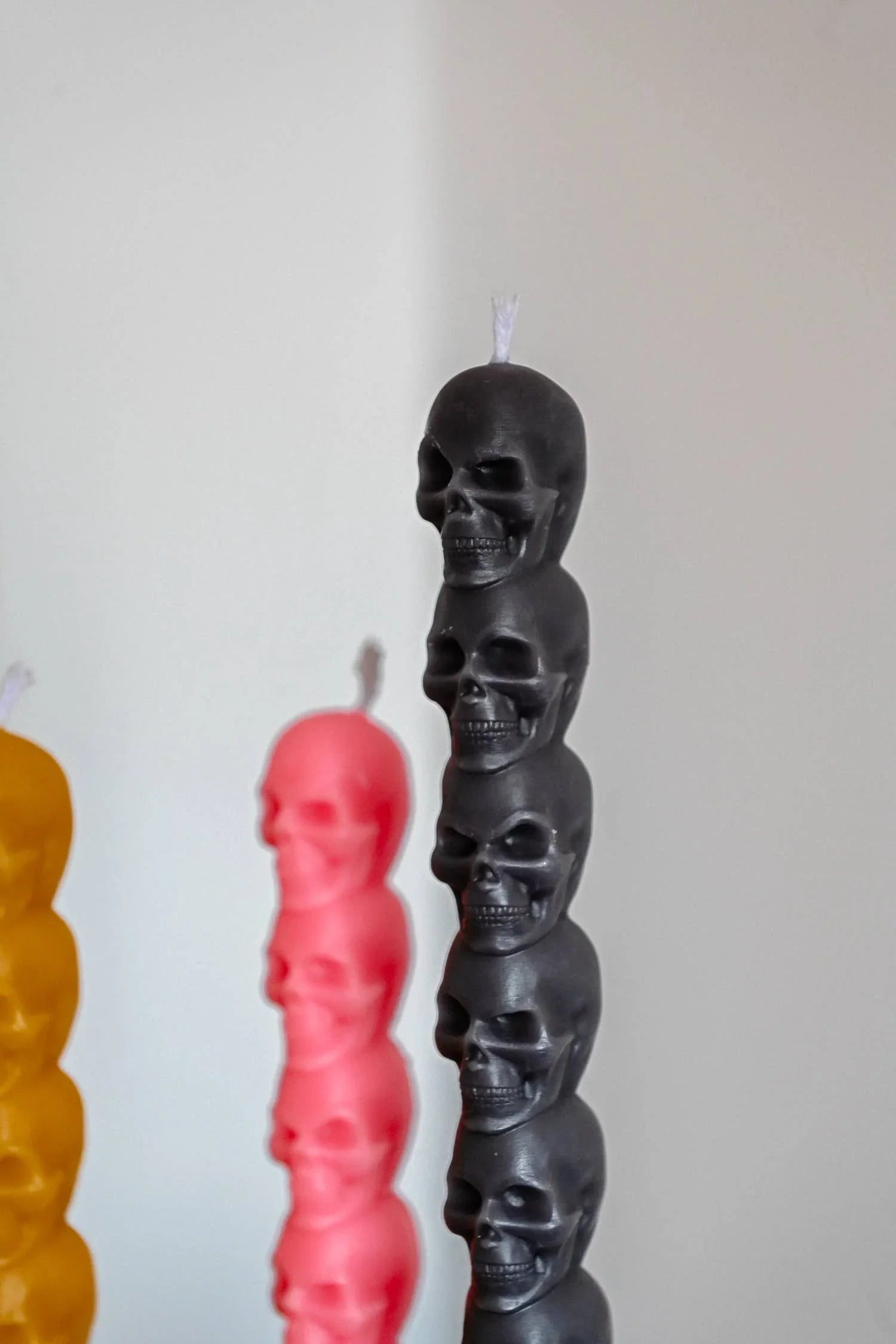 CandleHand black skull candle, wax, sculpted, with yellow and pink variants in background.