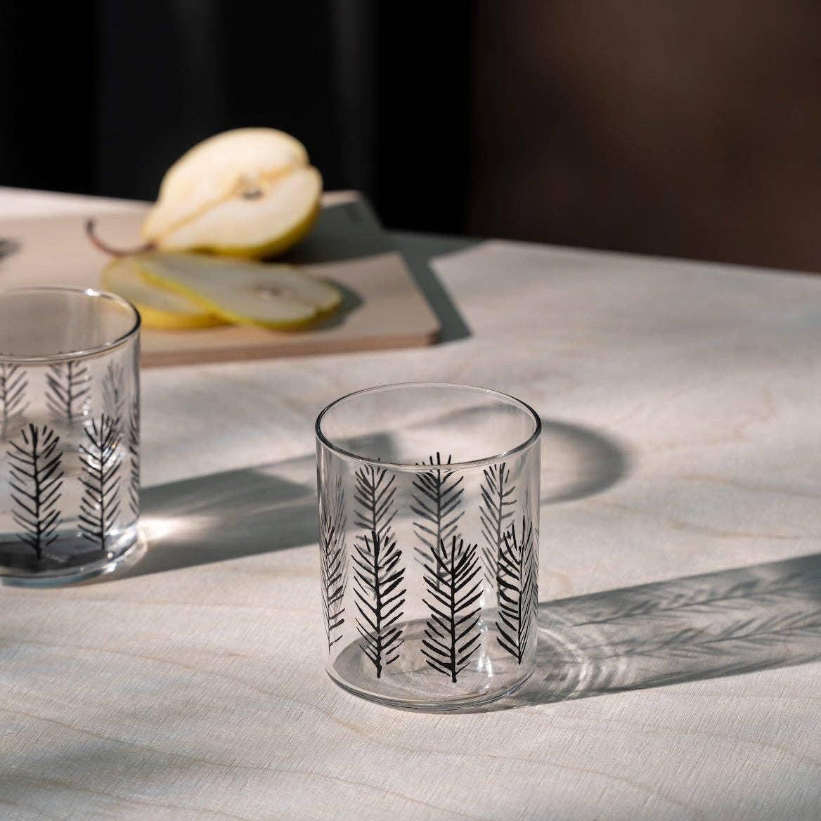 Ferm Living clear glass tumbler with black botanical pattern on light table, pear slices in background.
