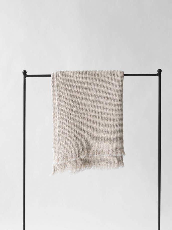 Baina beige textured cotton towel with fringe detailing hanging on black rack