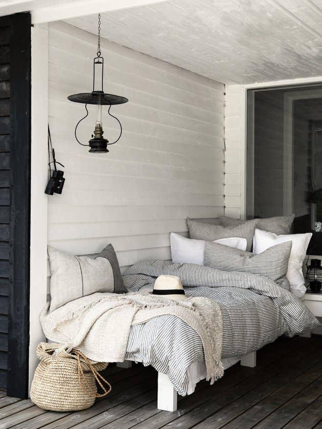 Cozy outdoor daybed with striped cotton bedding, linen throw, woven basket, and neutral tones