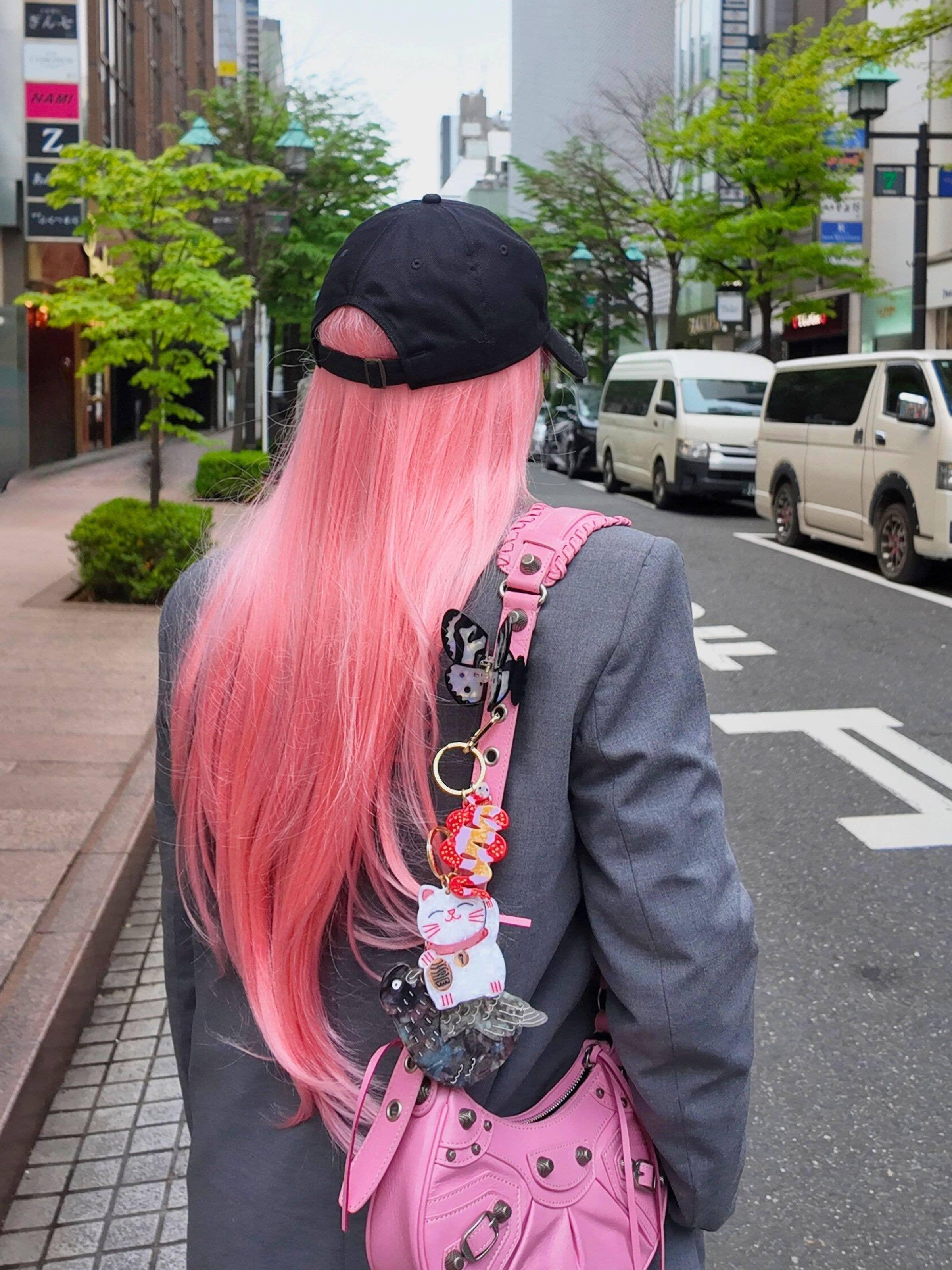 Balenciaga pink leather handbag with cat and bear keychains, gray blazer, person with long pink hair