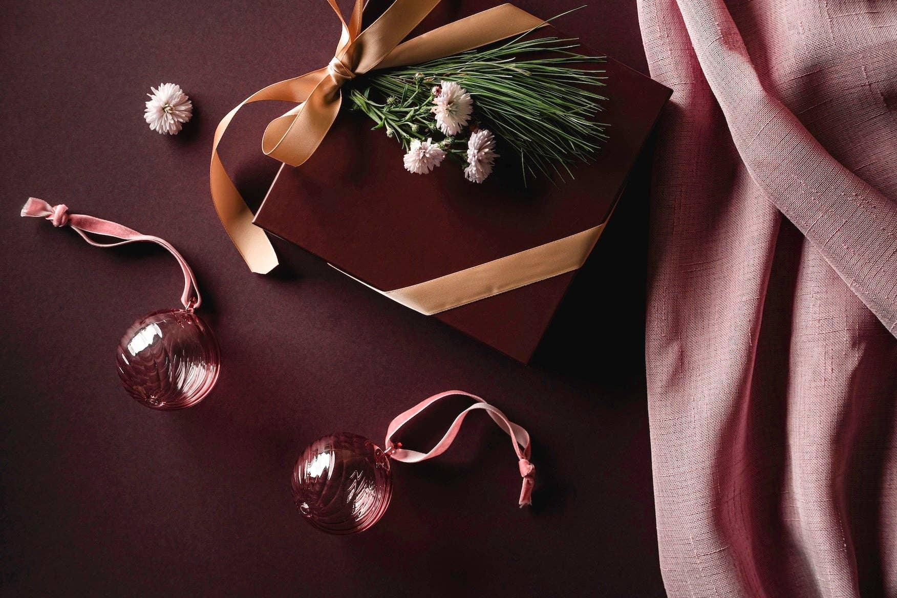 Elegant gift box with gold ribbon, pine and flowers, pink glass ornaments, mauve fabric