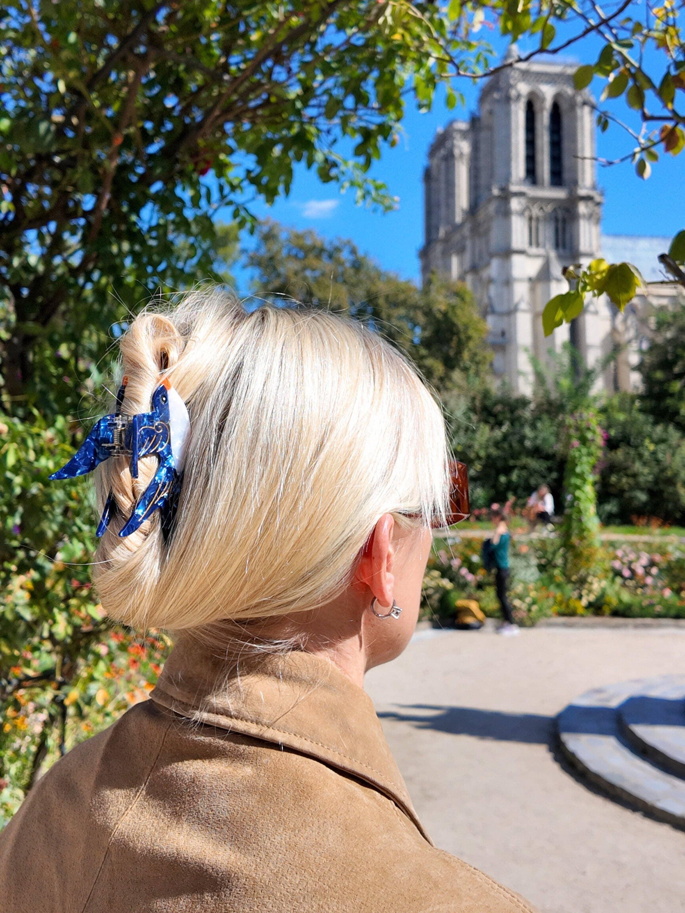 Epona Valley blue acetate hair claw clip in blonde hair, outdoors near Notre-Dame Cathedral