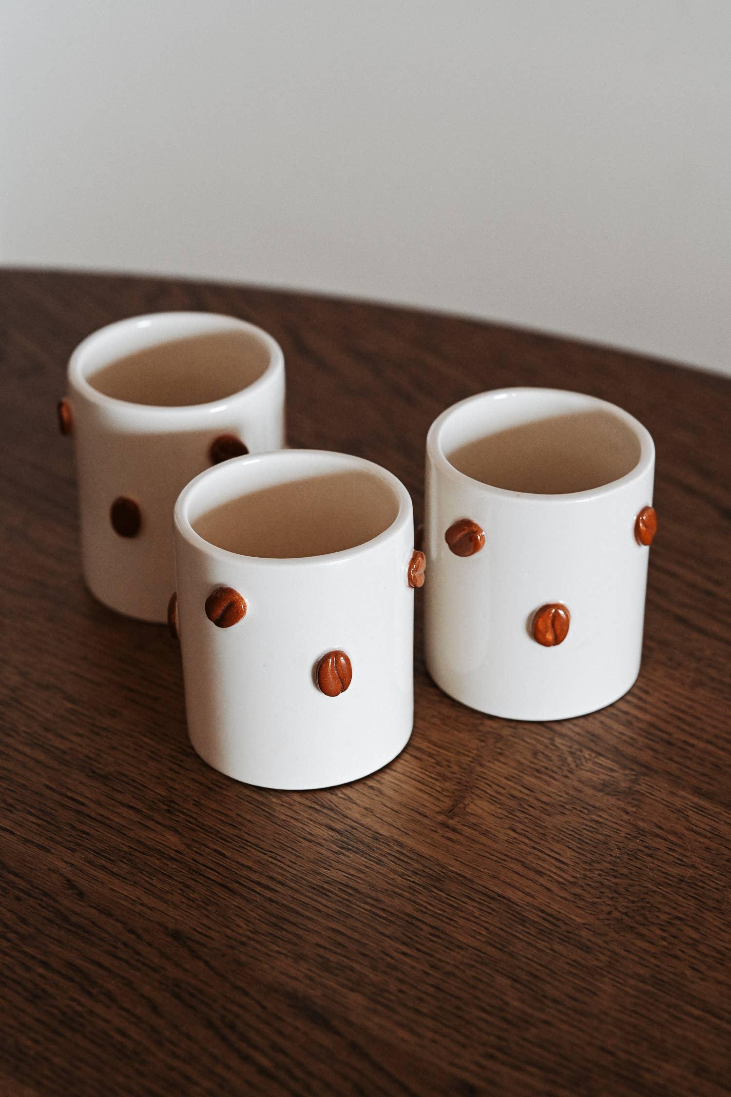 Claymen ceramic mugs with brown coffee bean accents, white stoneware on wood table