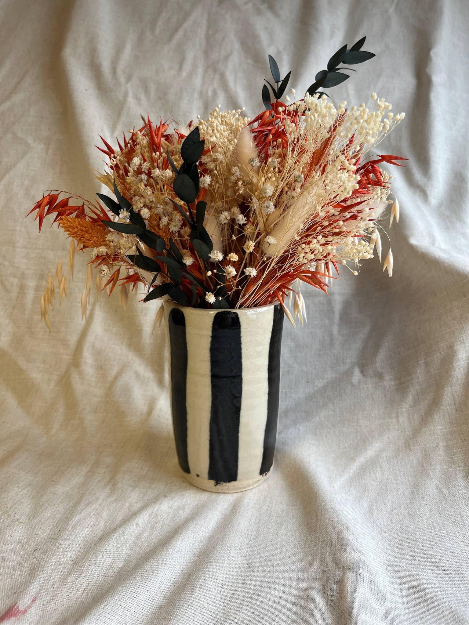 Handmade ceramic striped vase with dried floral arrangement in red, cream and black tones.