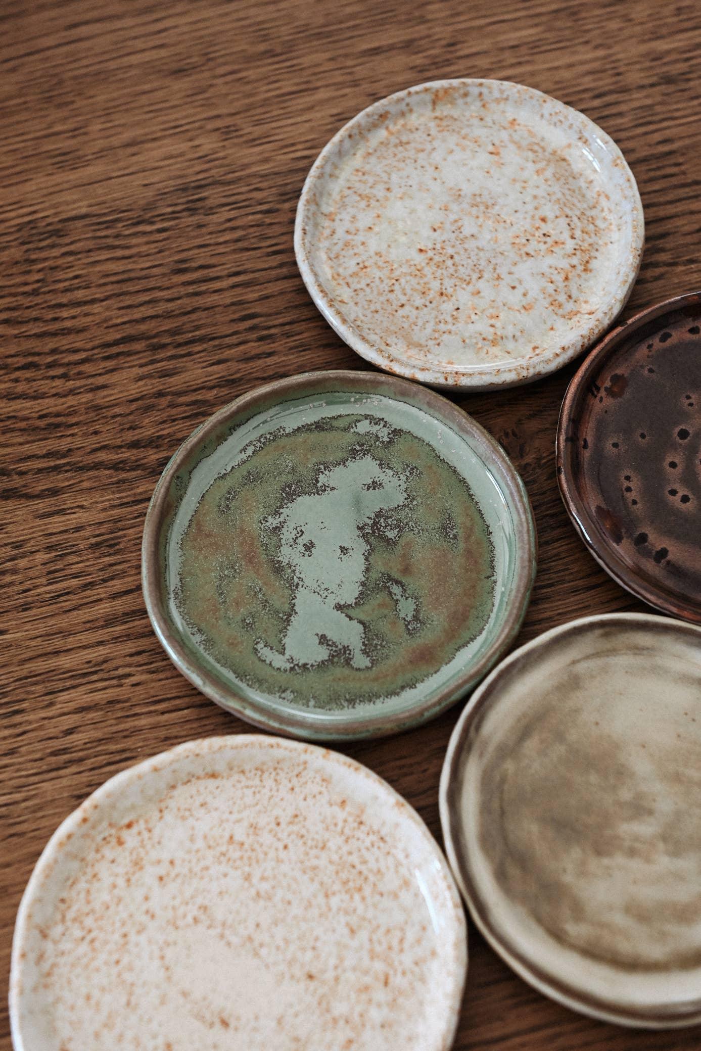 Akomeya ceramic small plates, speckled and glazed, assorted earth tones, on wood table