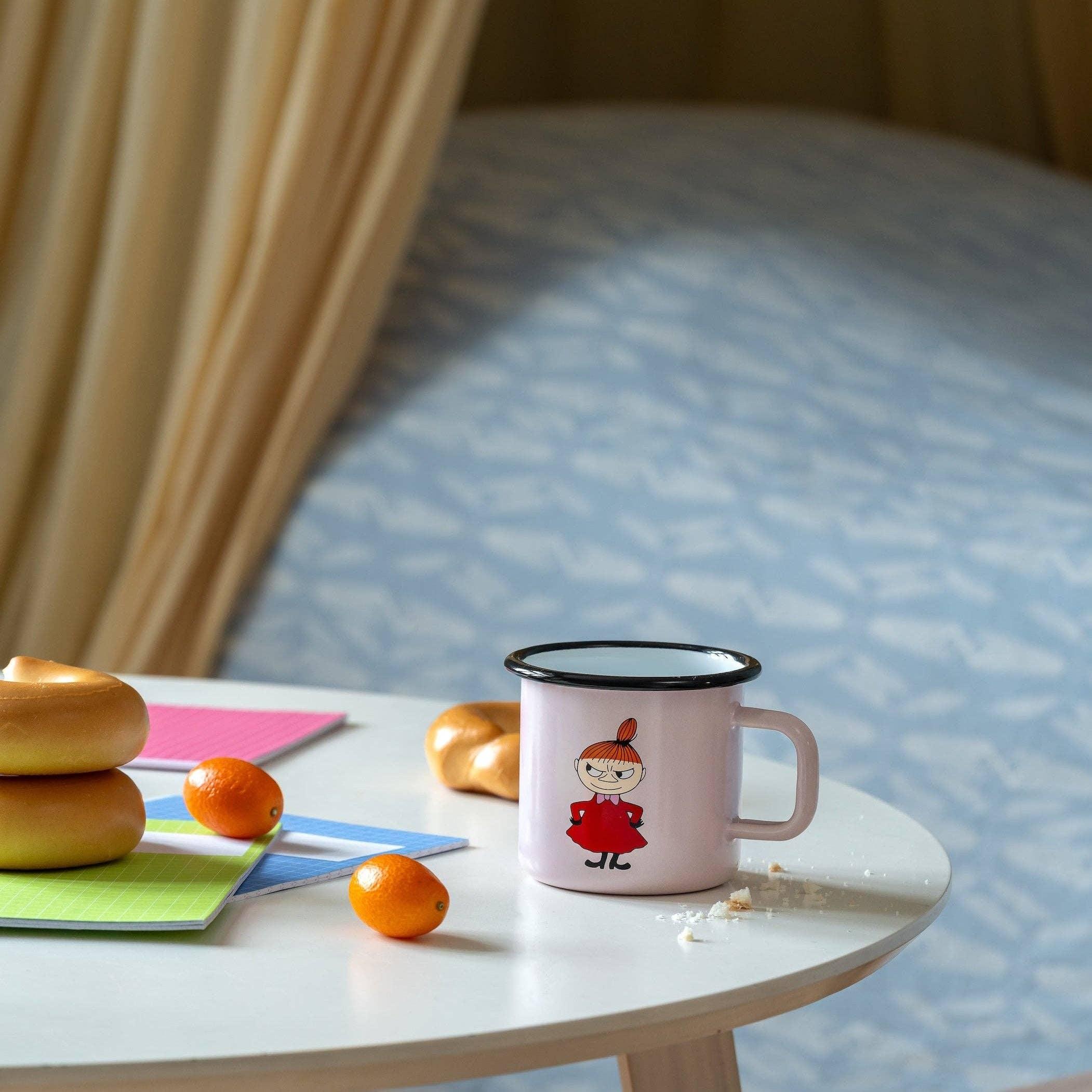 Moomin pink enamel mug with Little My illustration on white table with bagels and kumquats