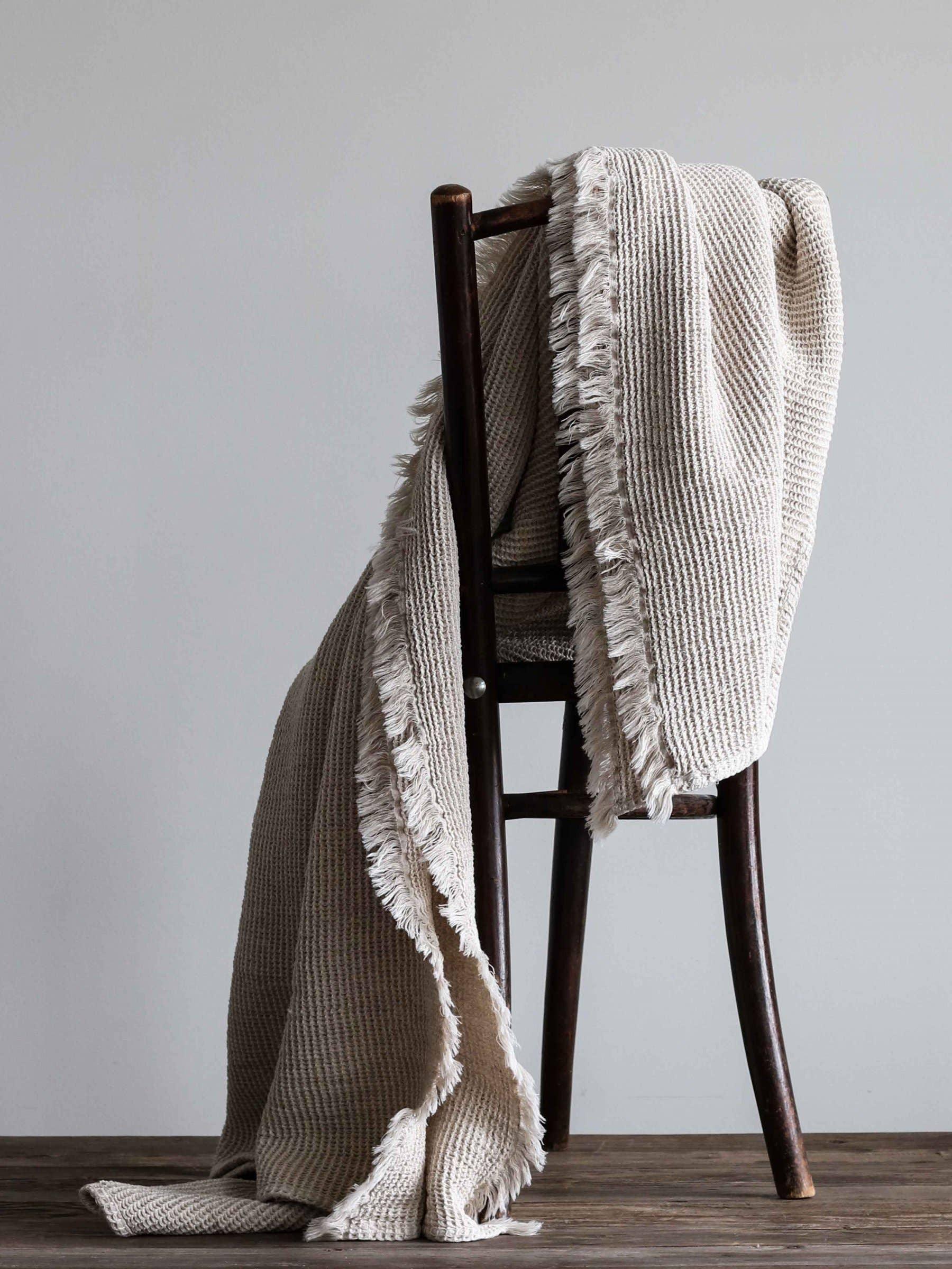 House No.23 beige cotton throw blanket with fringed edges draped on dark wooden chair