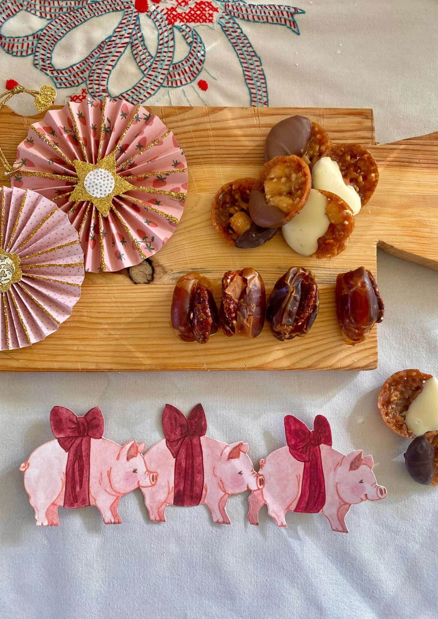 Handmade pink paper rosettes, chocolate-dipped cookies, and stuffed dates on wooden board