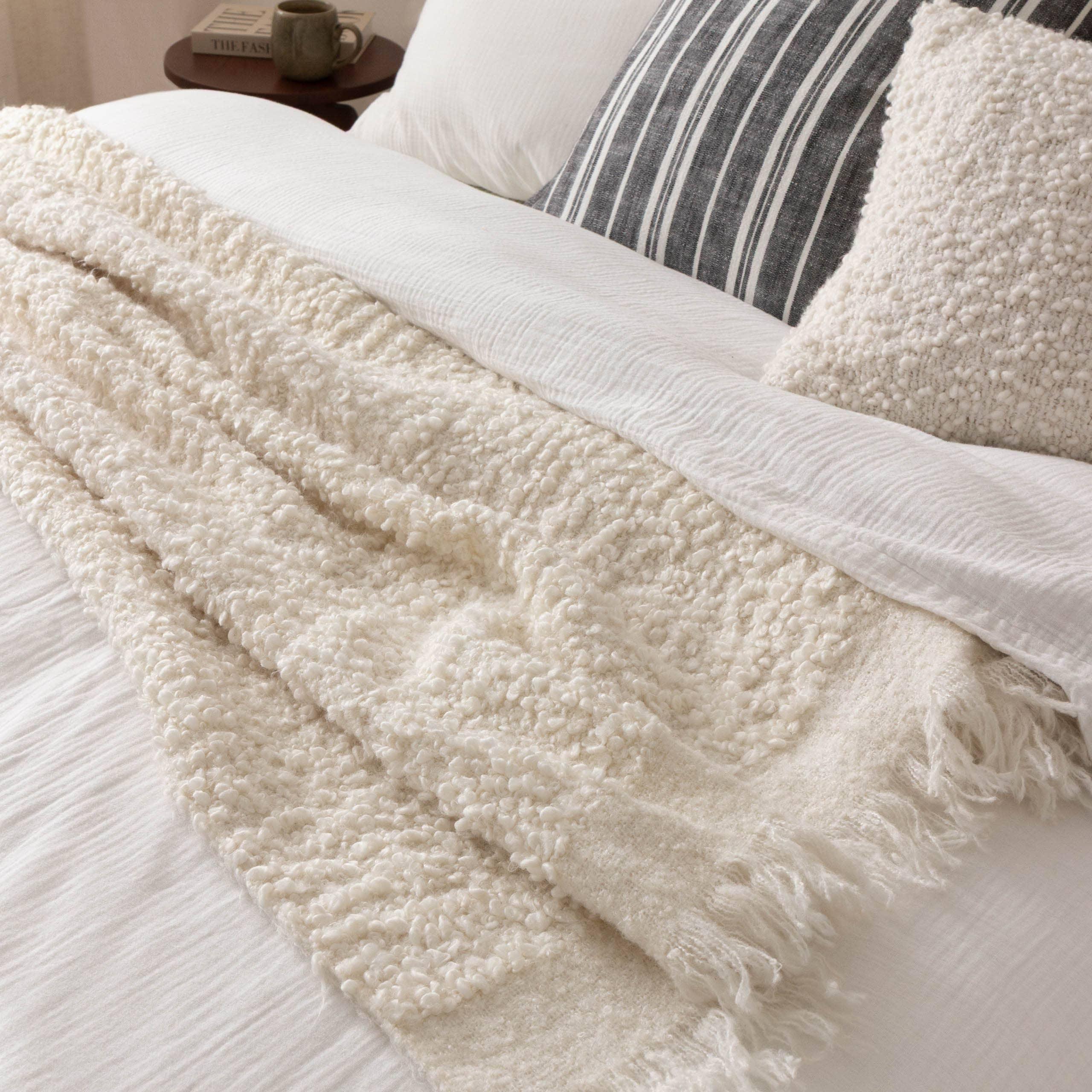 Casa Boho ivory boucle throw blanket, textured cotton, on a white bed with striped pillow