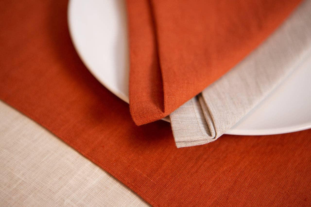 Linen Tales linen napkins in rust and beige on white plate with rust table runner