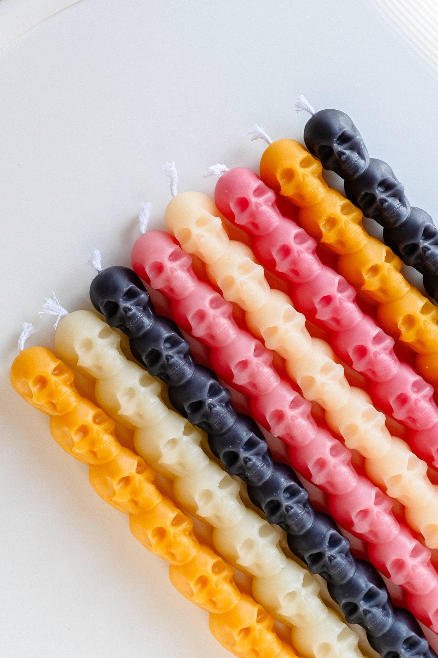 You, Me & Bones skull candles in black, yellow, cream, and pink soy wax, arranged on white background