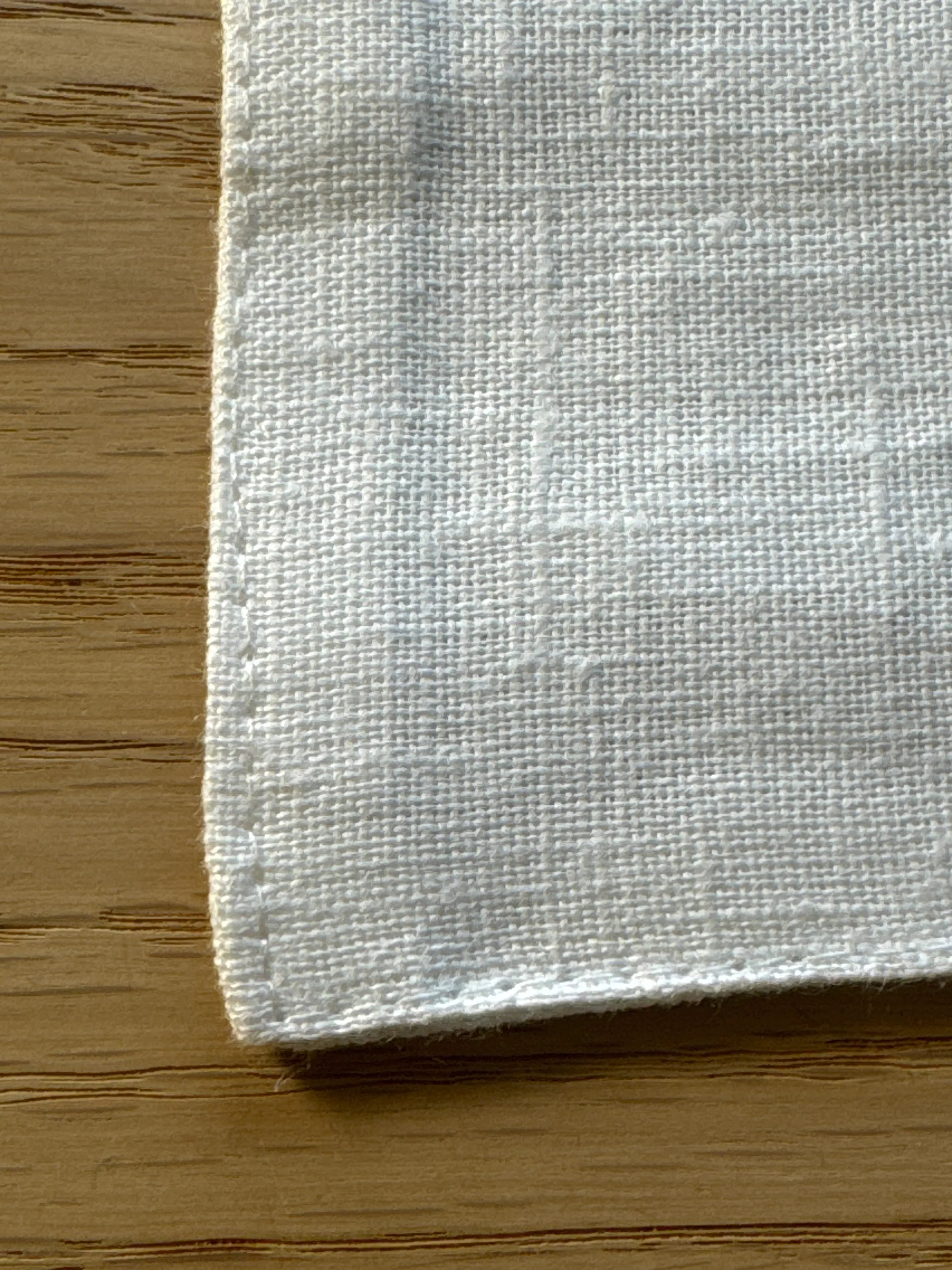 Gilded Olive pure linen white napkin on natural wood surface, close-up detail