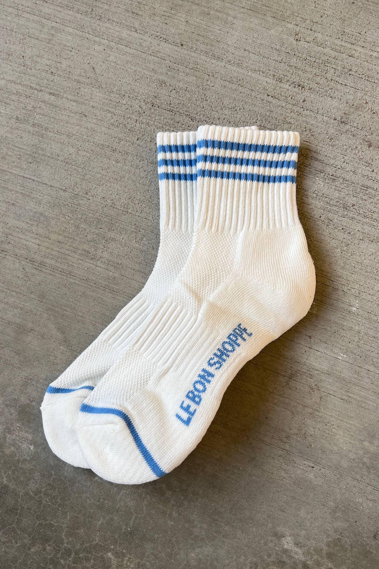 Le Bon Shoppe white cotton crew socks with blue stripes and branding on a concrete surface