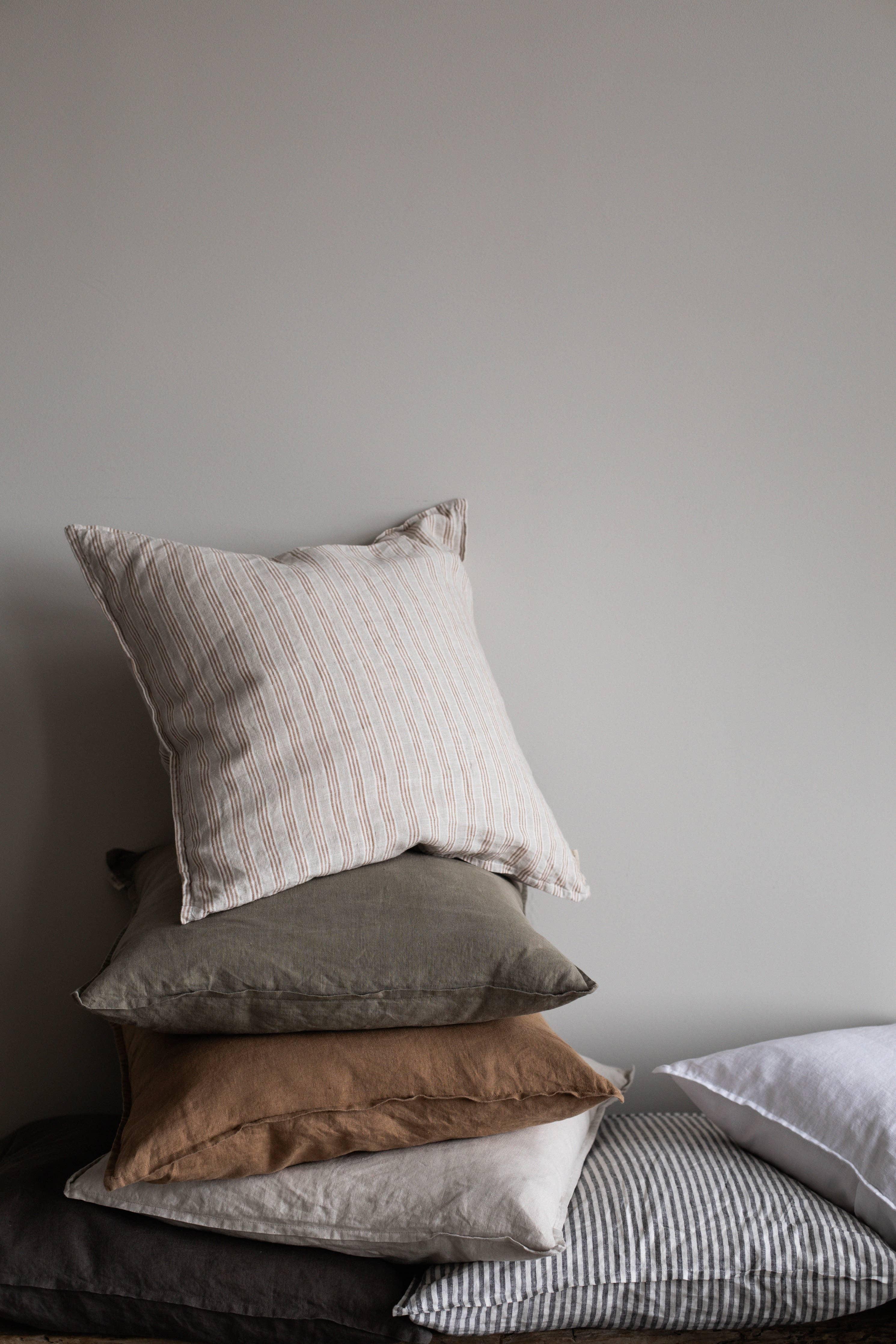 Midnatt premium linen pillow covers in muted earth and striped colors, neatly stacked