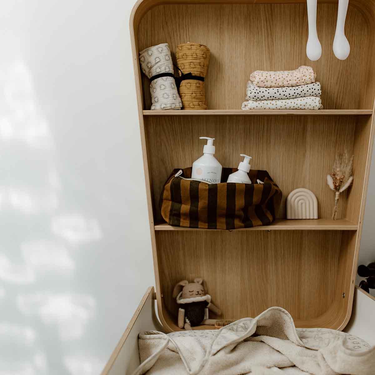 Wooden Olli Ella nursery shelf with organic cotton baby blankets and lotion, neutral colors