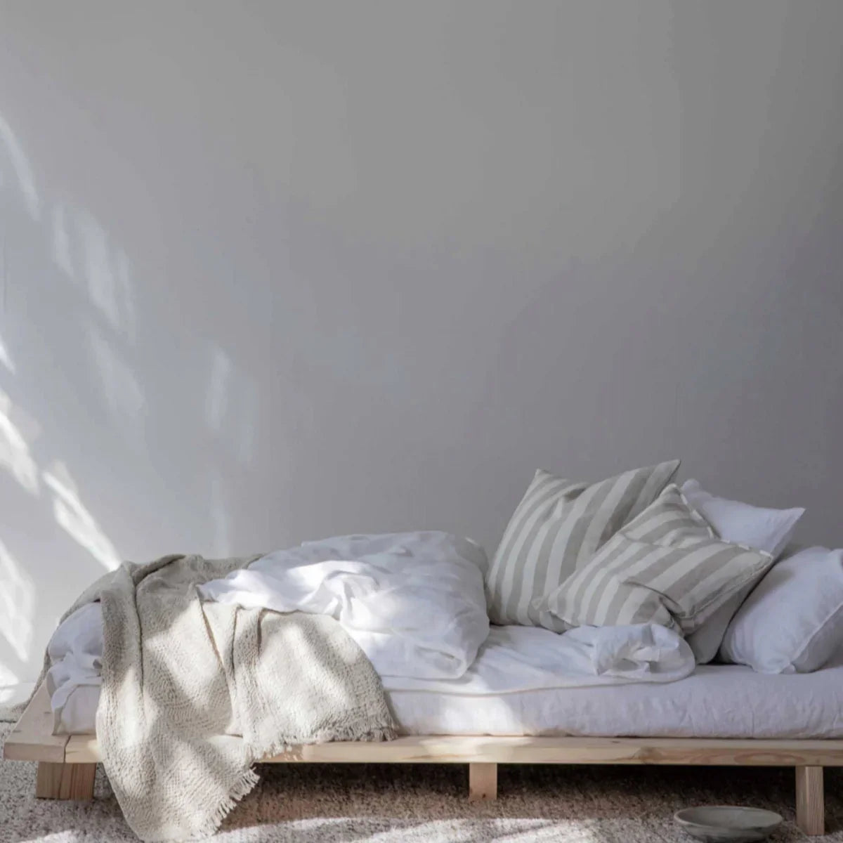 Toko Japanese-style natural wood platform bed with white linen, striped pillows, and beige throw blanket