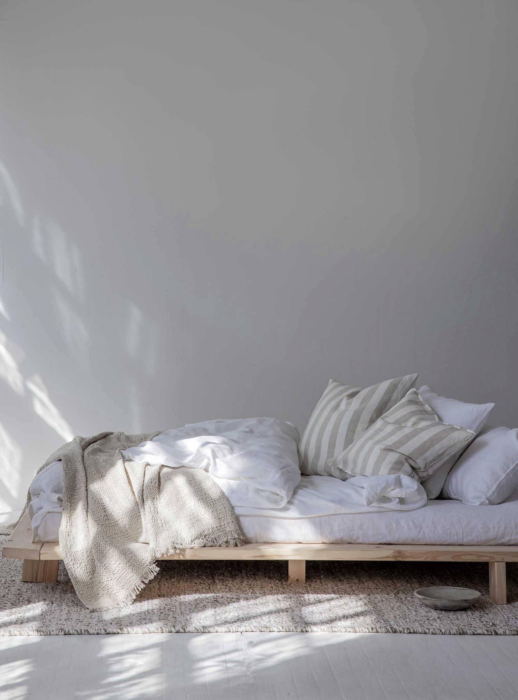 TOMOKO minimalist wooden bed with white linen, striped cotton pillows, neutral throw blanket