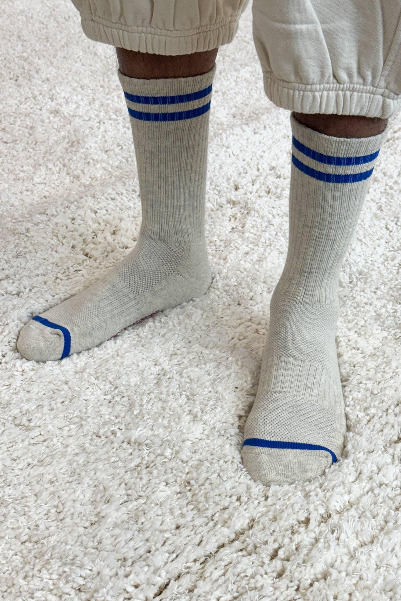 SHASHI classic crew socks in beige cotton with blue stripes, worn on a textured white rug