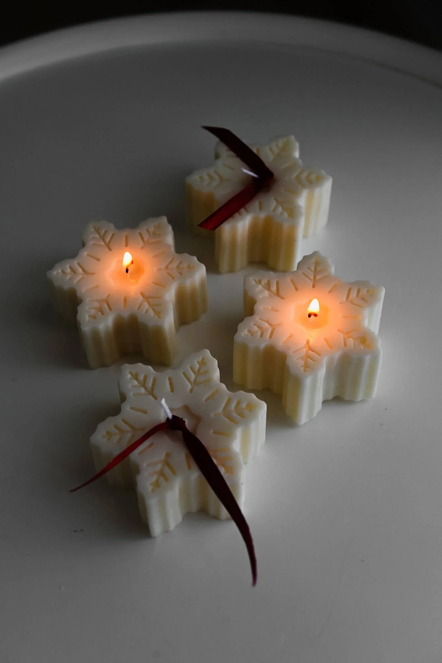 Three Ivory Studio snowflake-shaped soy candles, cream color, with red ribbon detail