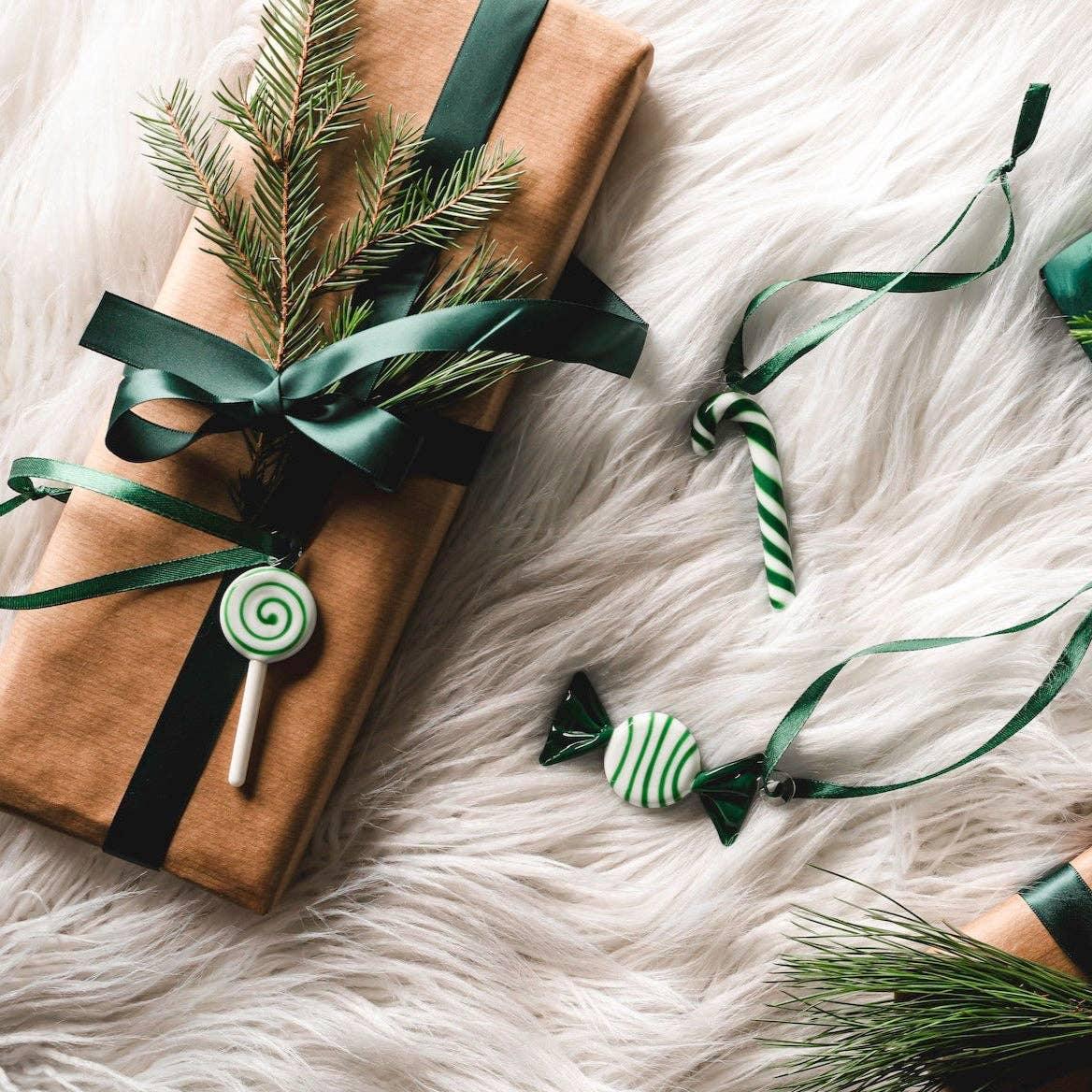 Gift wrapped in brown paper with green ribbon, fir branch, lollipop ornament, on white fur