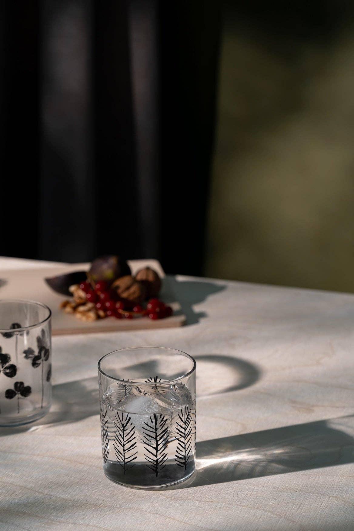 HAY glass tumbler with black botanical print on clear glass, set on a light table.