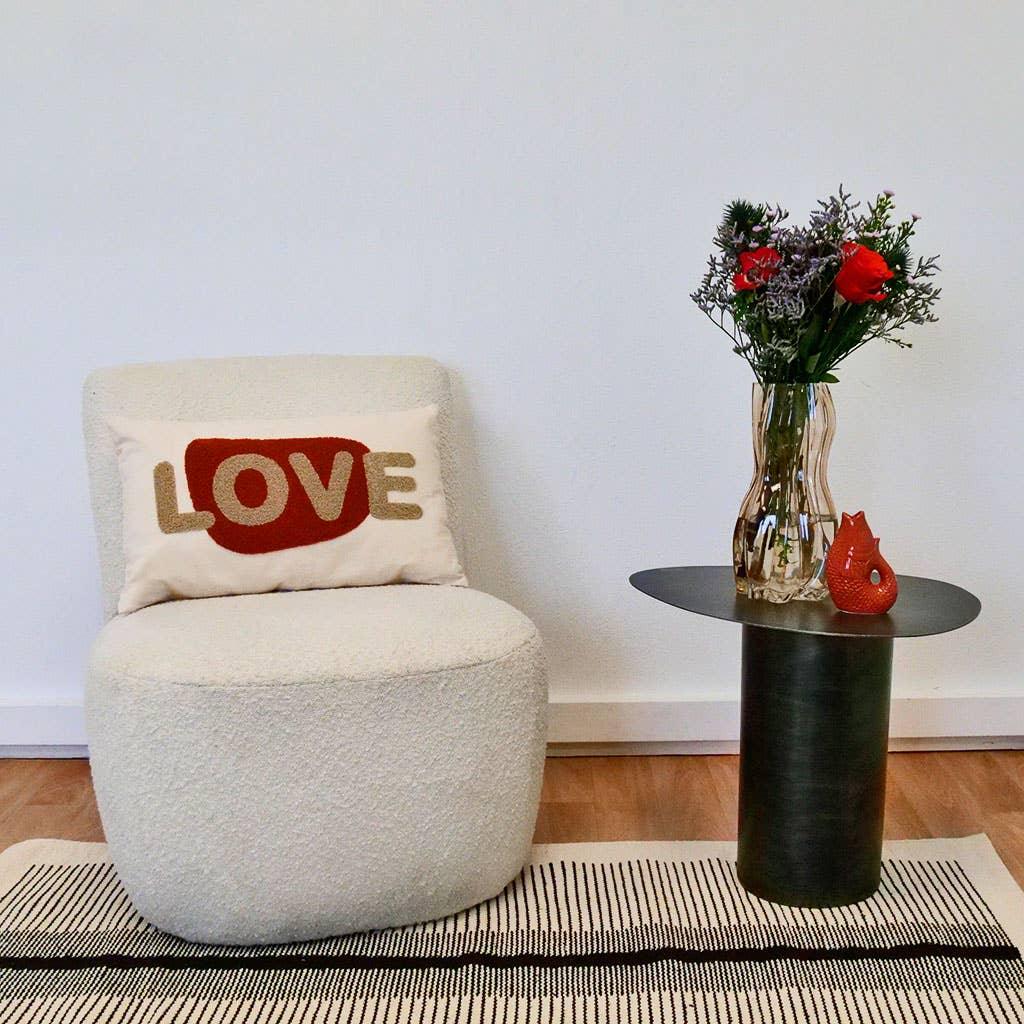 LOVE pillow on cream boucle chair beside black metal side table with glass vase and flowers