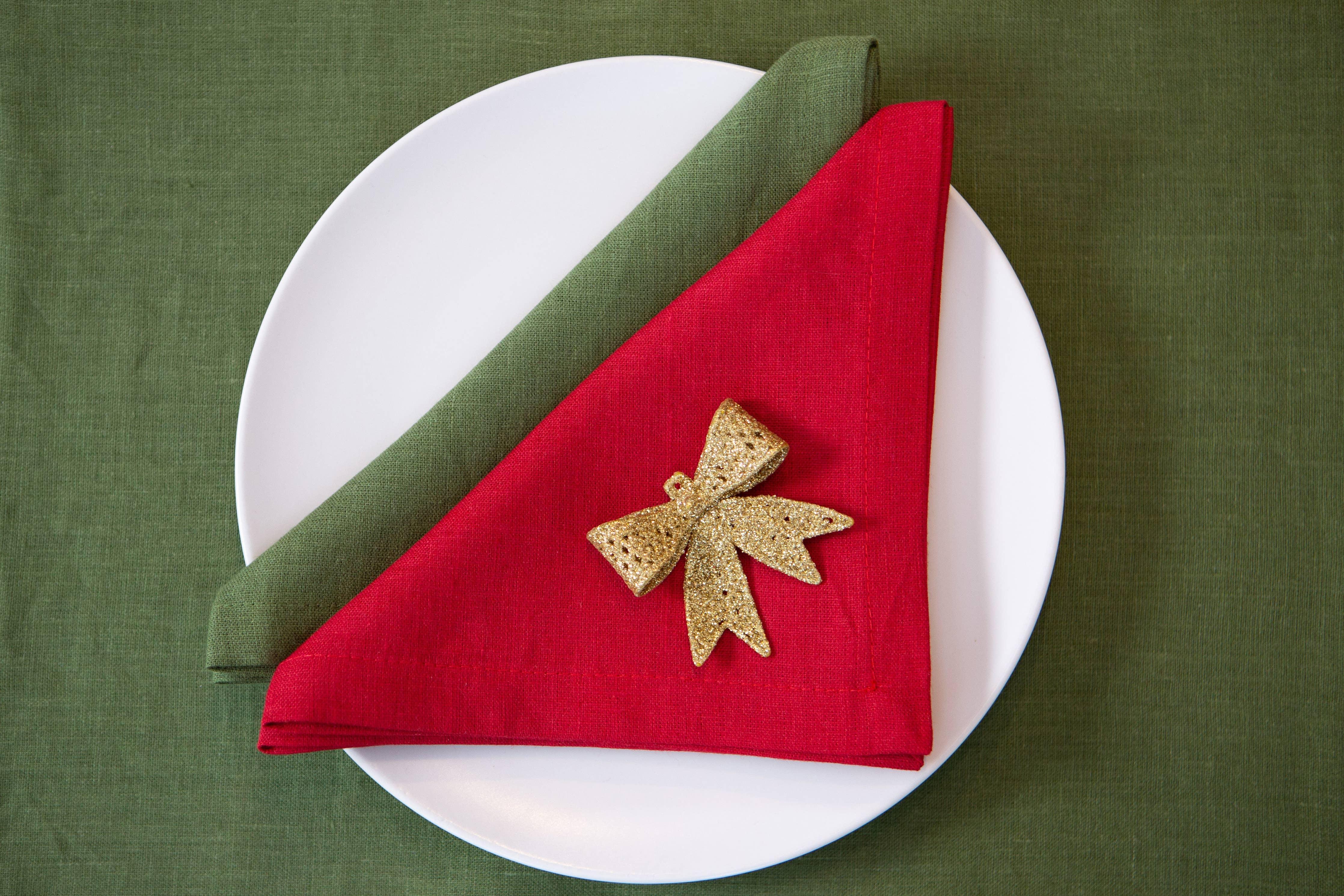 MagicLinen linen napkins in red and green with gold bow, on white plate, holiday table setting