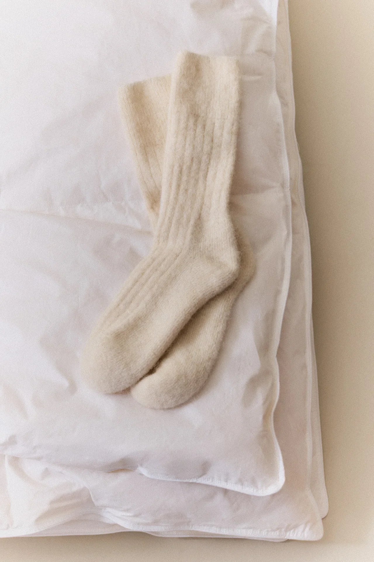 Deiji Studios cream alpaca wool socks on white bedding, premium soft knit loungewear