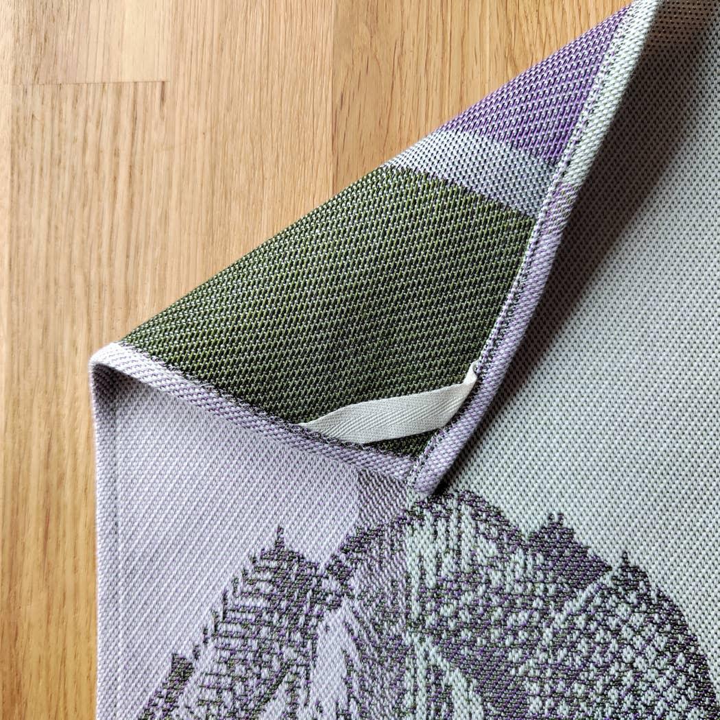 Nusantara woven cotton textile in green and lavender tones on wood surface