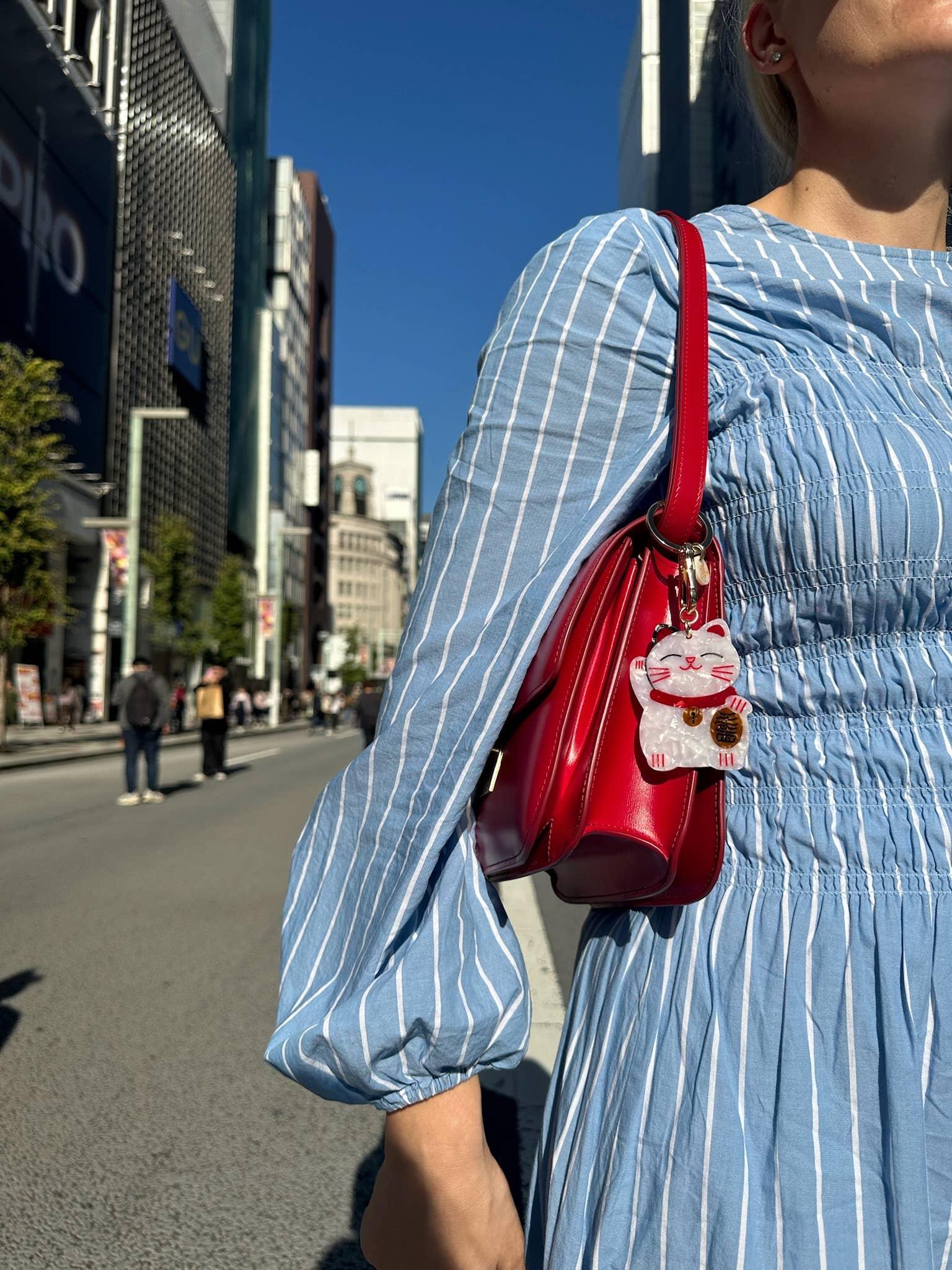 PREO red leather handbag with acrylic lucky cat charm, blue striped dress in city street