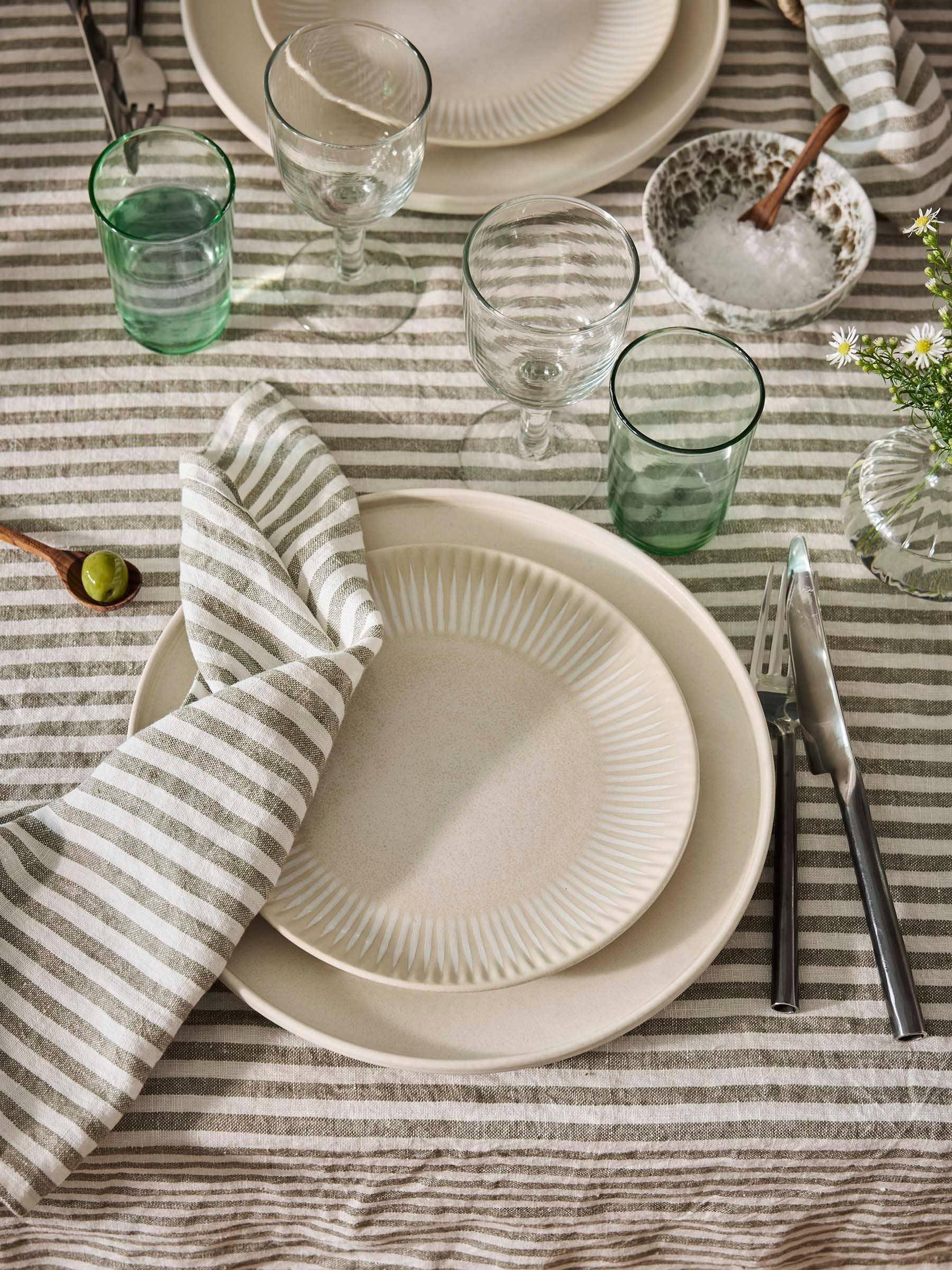 Fog Linen Work linen striped tablecloth, ceramic plates, glassware, and cutlery on table
