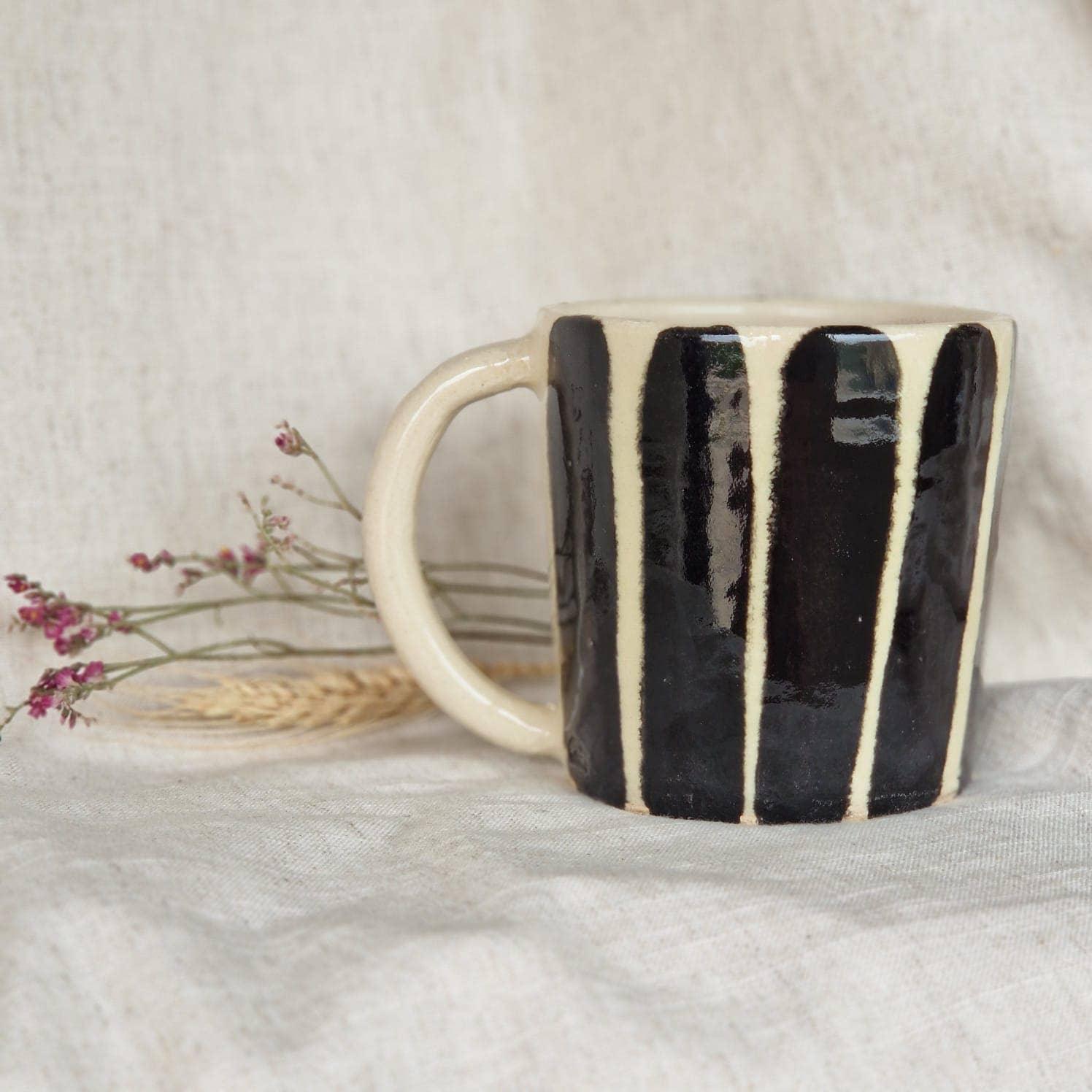 IKKARI handmade ceramic mug, black and cream striped, on linen fabric with dried flowers