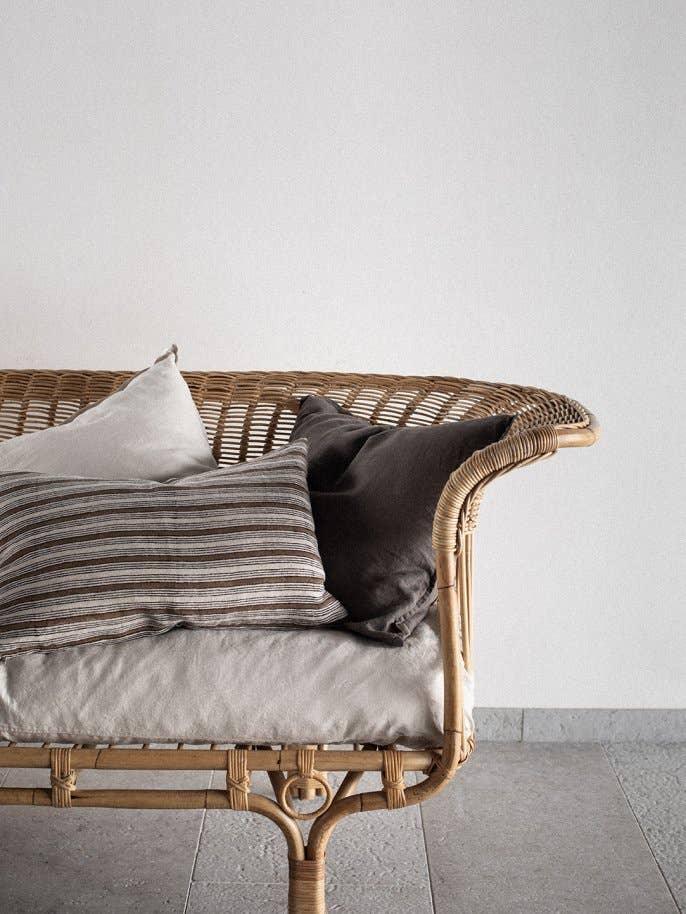 Tine K Home rattan bench with linen cushion and neutral throw pillows in a minimalist setting.