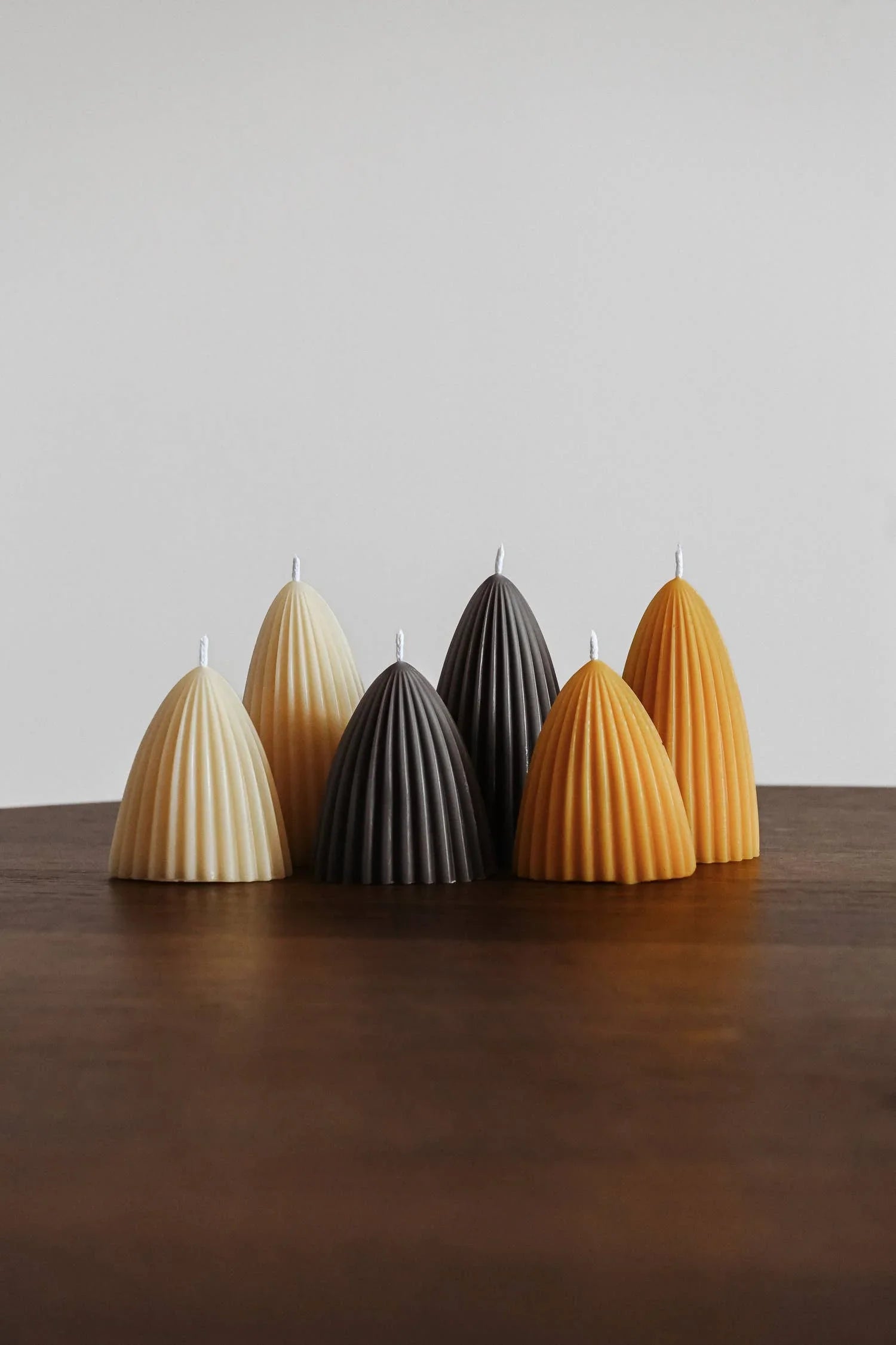 Osmology pleated beeswax candles in cream, grey, and amber on a wood table