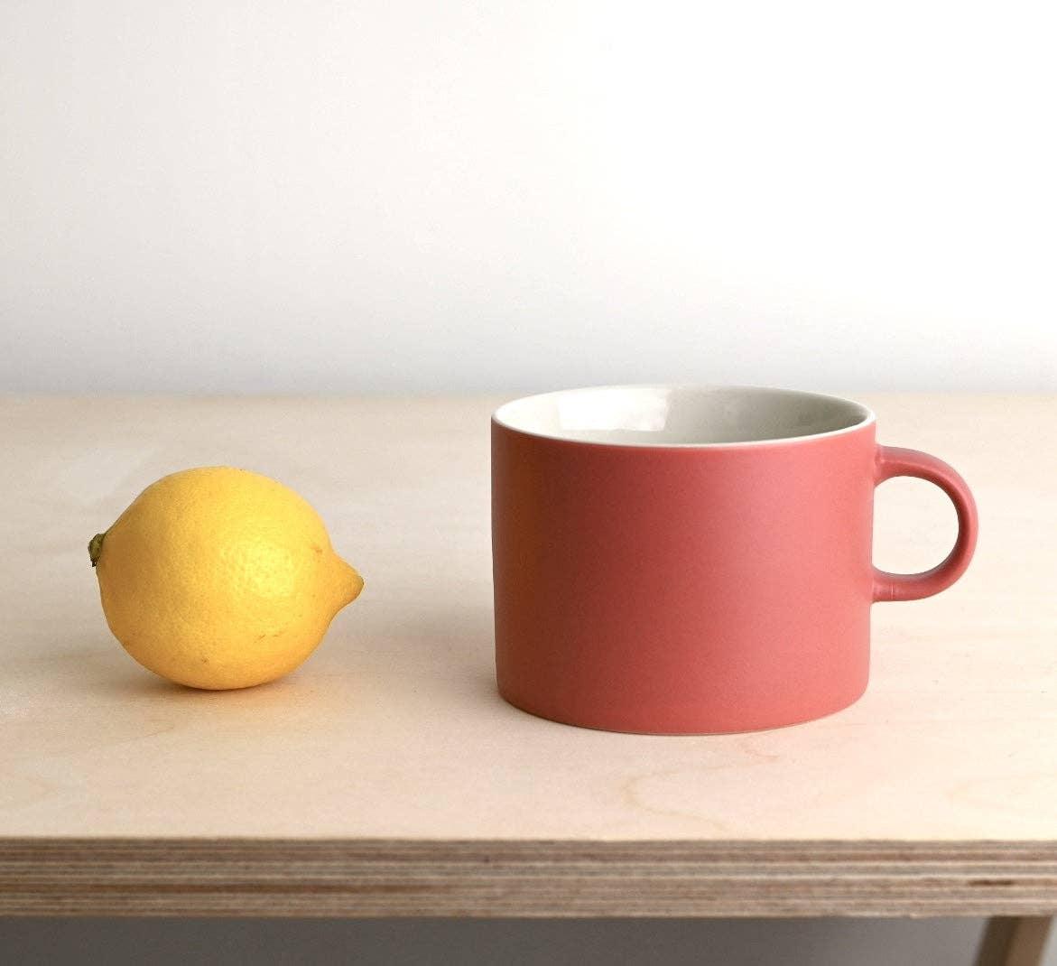 Kinto ceramic pink mug and yellow lemon on light wood table, minimalist setting