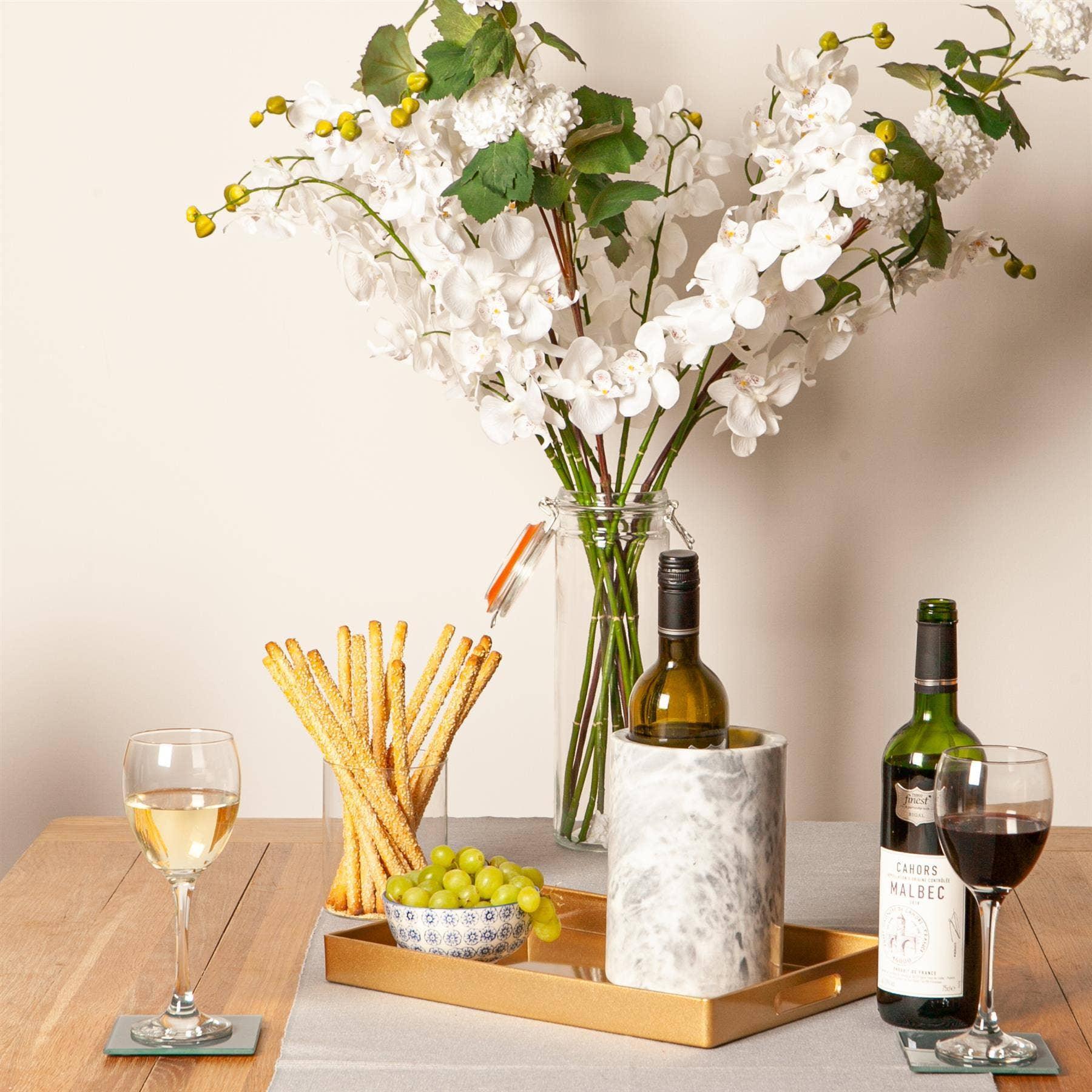 Premium table setting with marble wine cooler, gold tray, wine bottles, and white floral arrangement