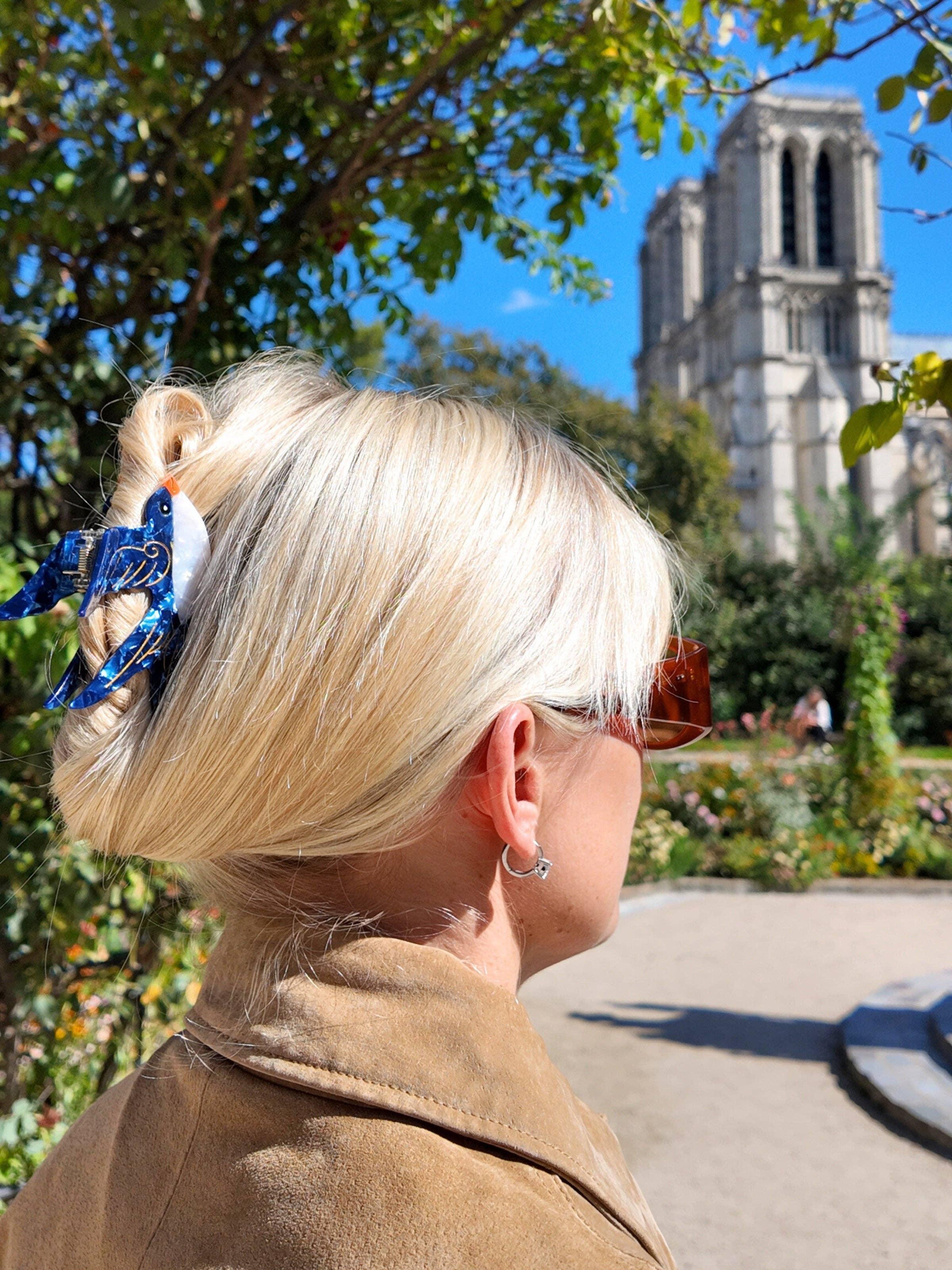 Nach Bijoux blue acetate bird hair clip in blonde hair, outdoors near historic building