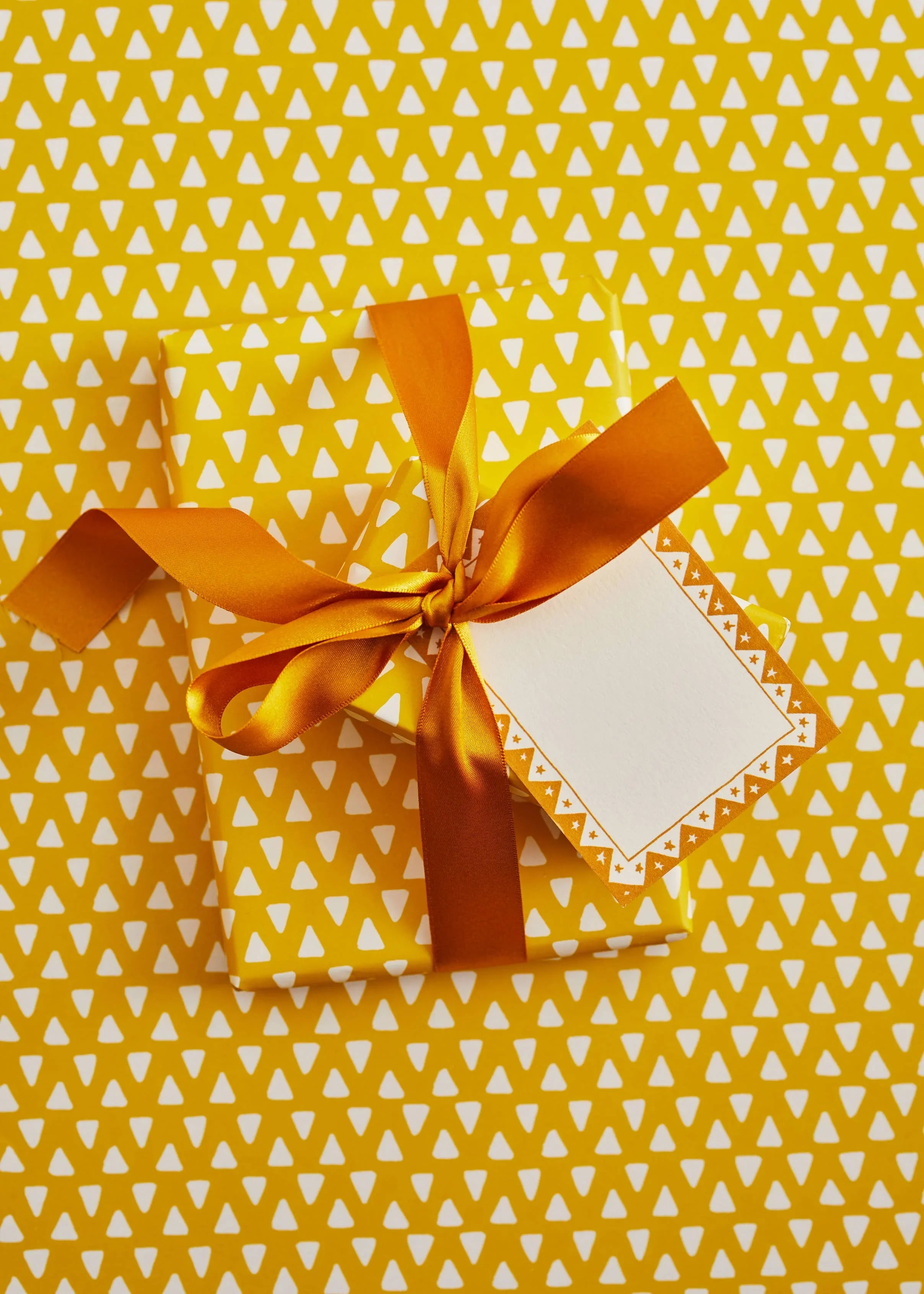 Premium gift box with orange satin ribbon, geometric gold and white wrapping paper, blank tag