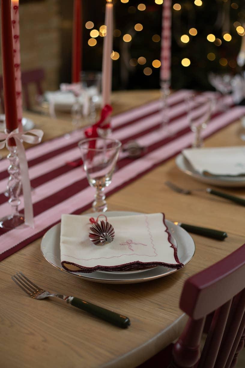 Issy Granger cotton napkin with burgundy trim on festive table setting, pink striped runner