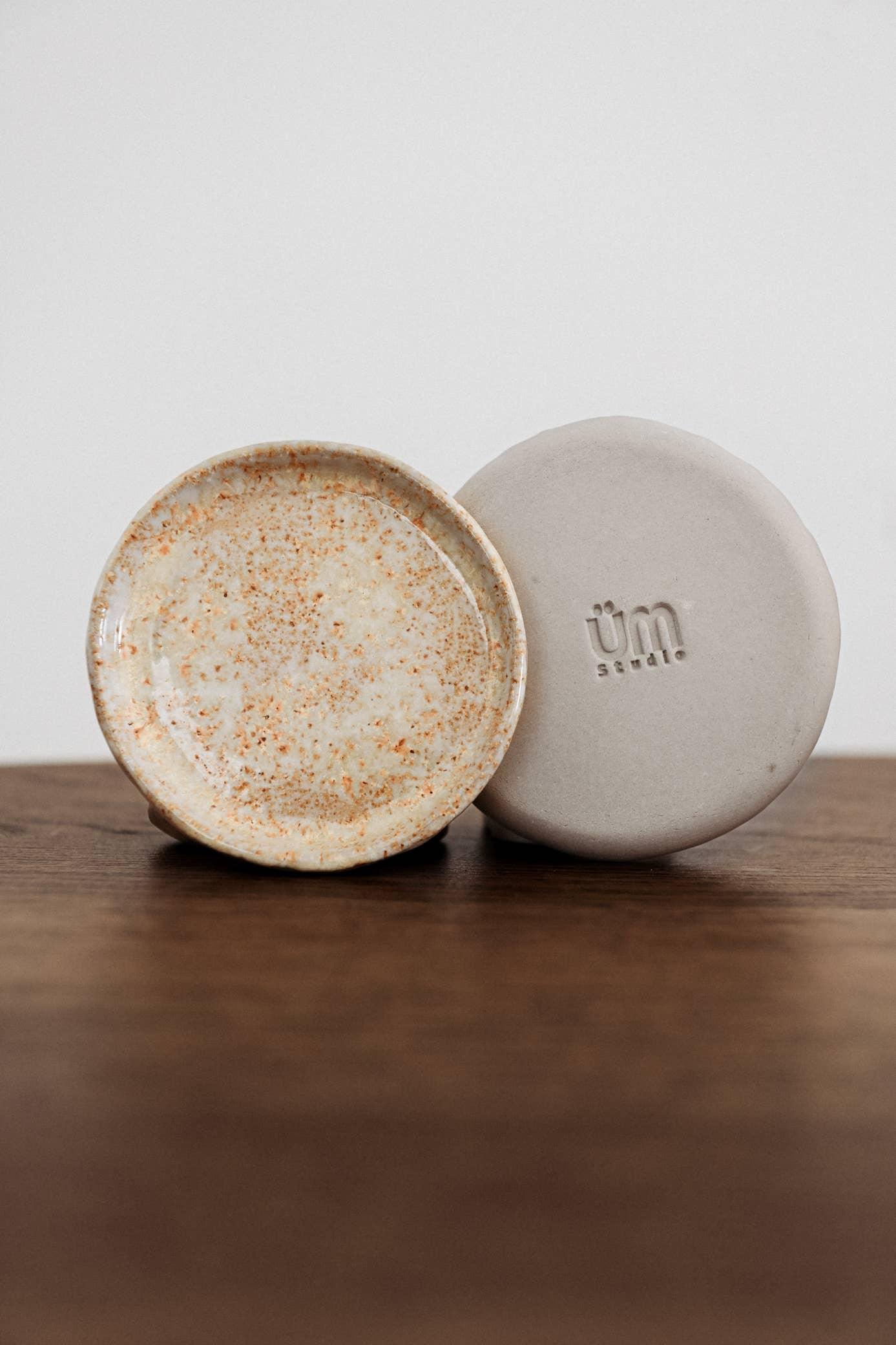 UM Studio ceramic dish, speckled glaze, beige and off-white, on wooden surface