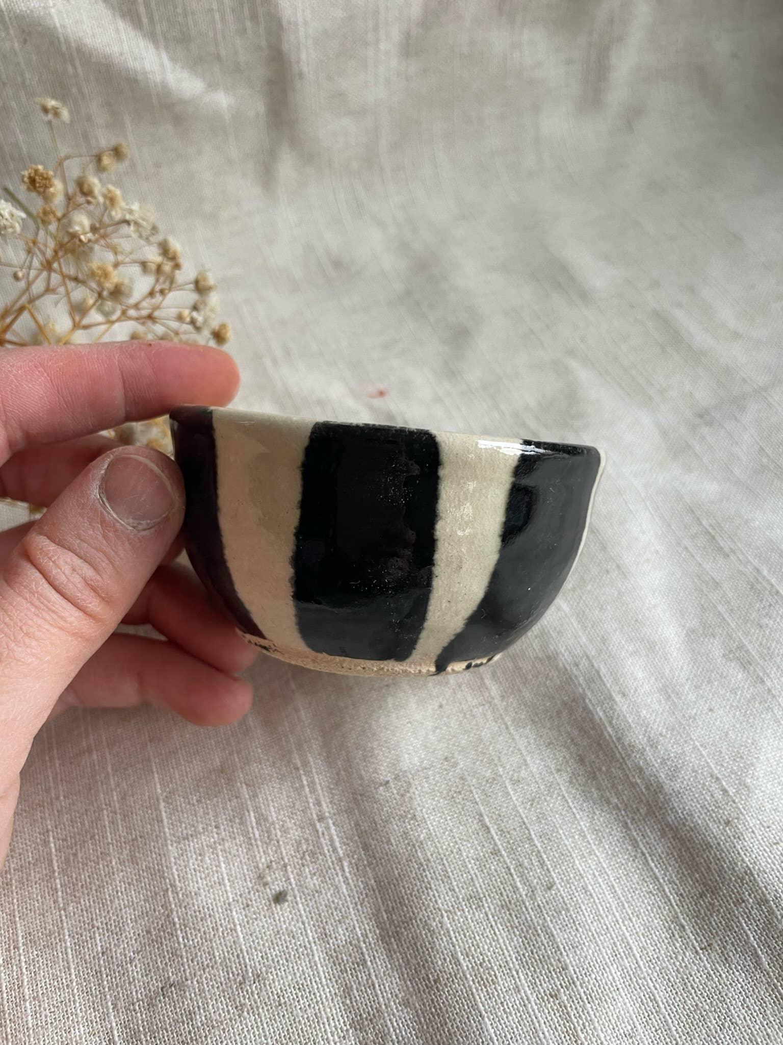 Hand holding black and cream striped ceramic bowl by wolftown on linen fabric