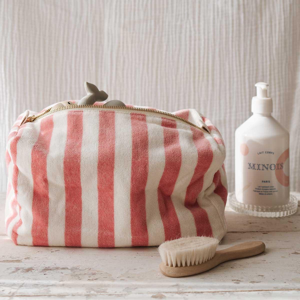 Minois Paris body lotion, striped cotton toiletry bag, and wooden brush on rustic table