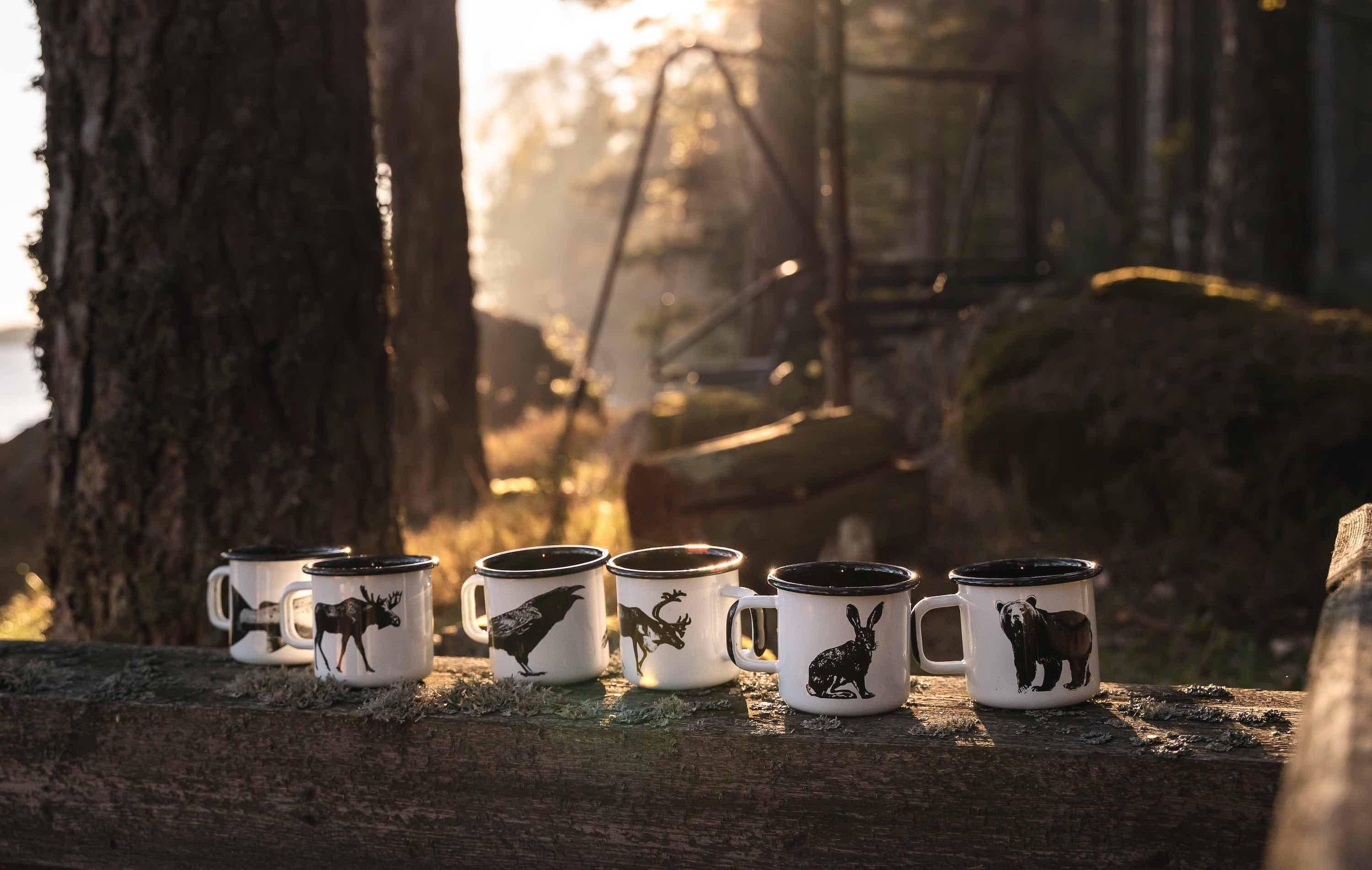 Polkra enamel mugs with black animal designs, white and black color, displayed outdoors on wood