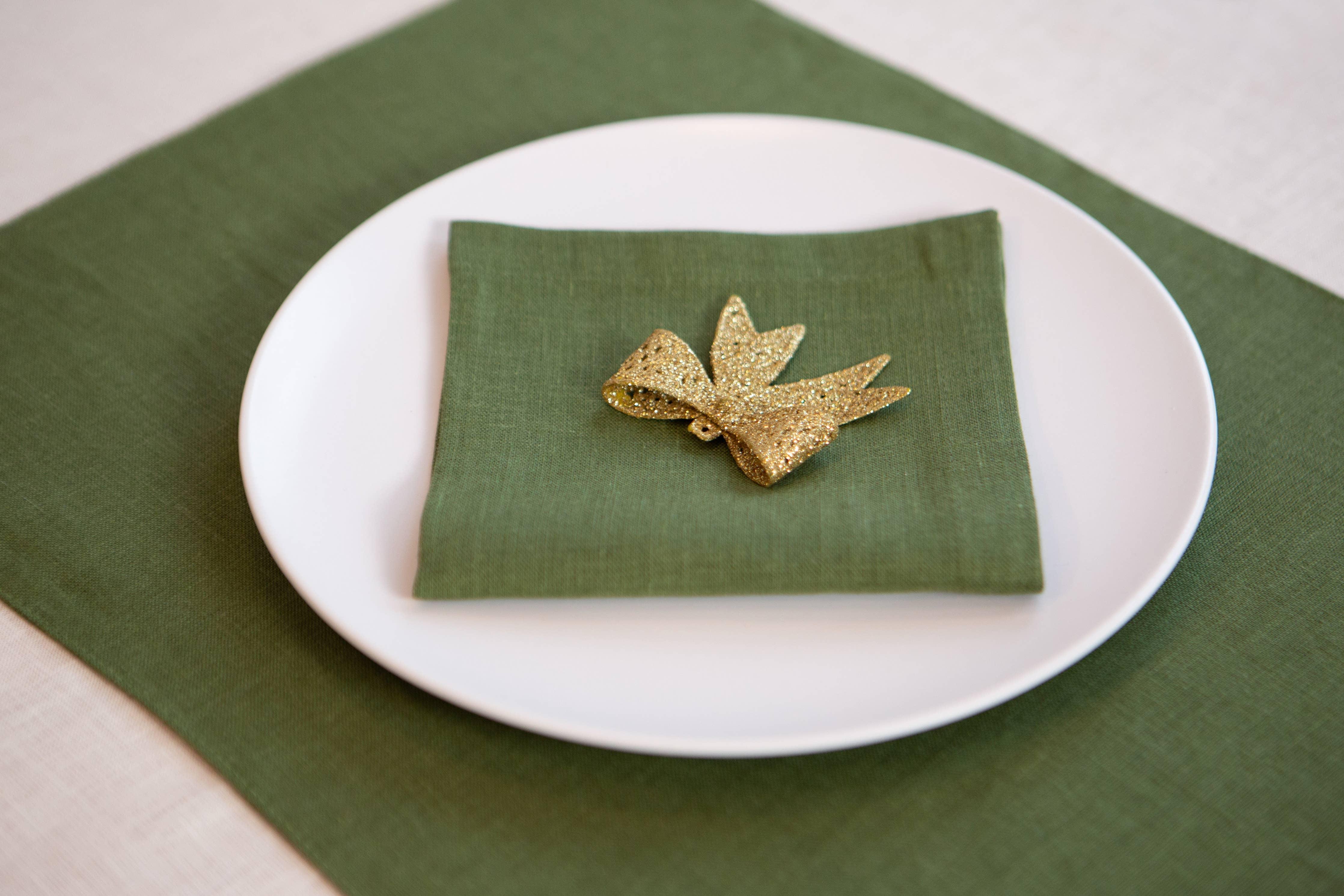 Linen Tales green linen napkin and placemat set with gold glitter bow on white plate