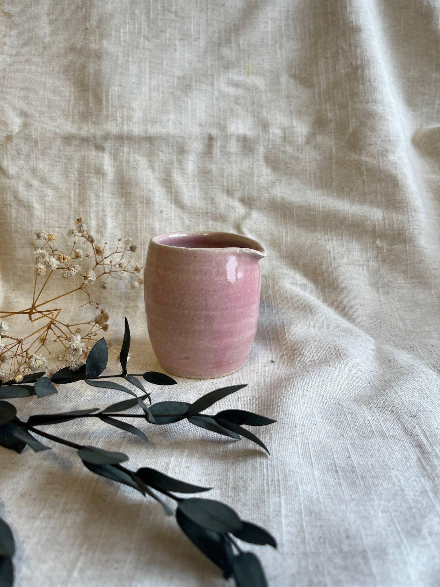 Handmade pink ceramic pitcher by Yido, displayed on linen with floral accents