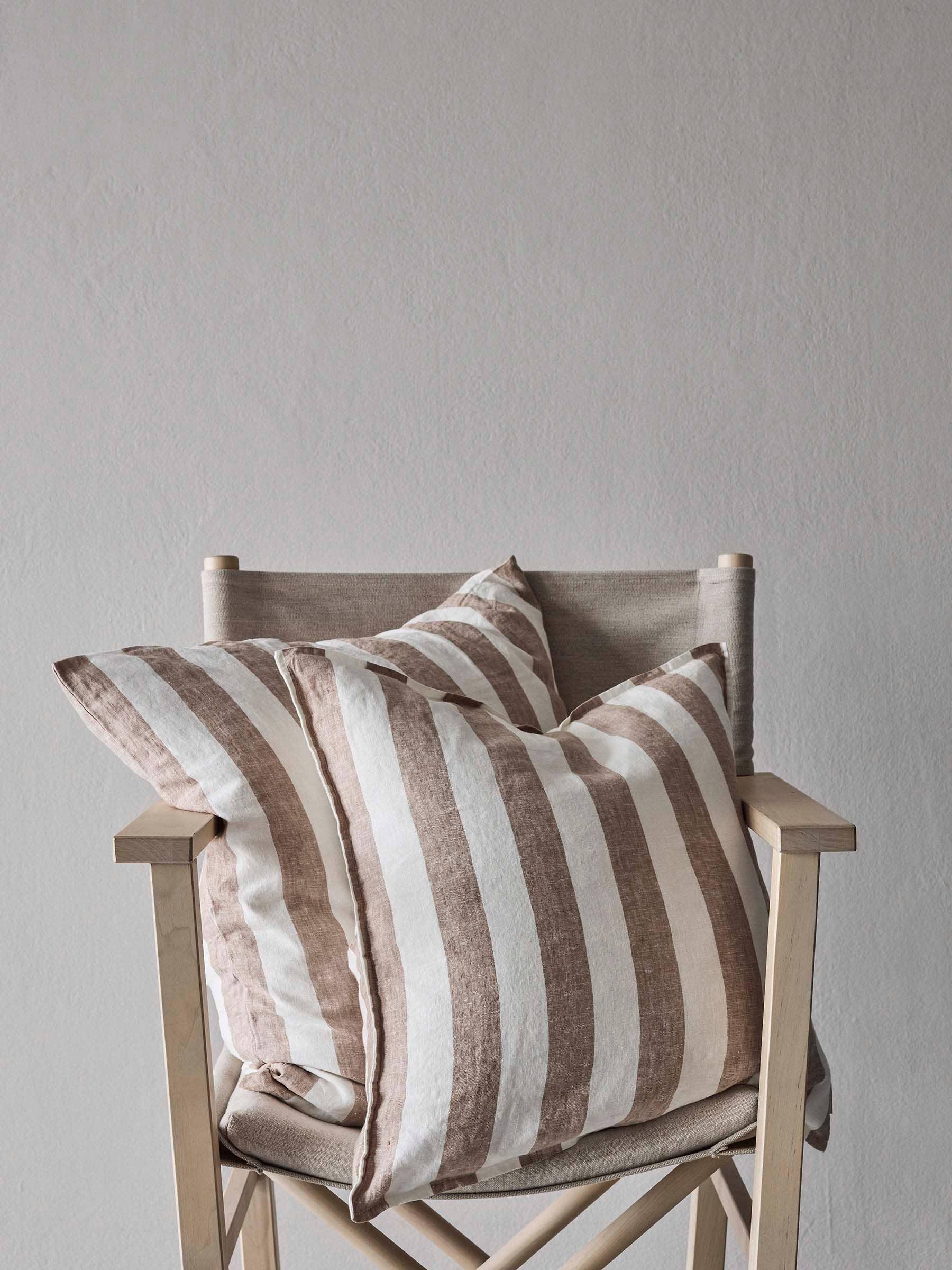 Tensira striped linen cushion covers in beige and white on a natural wooden chair